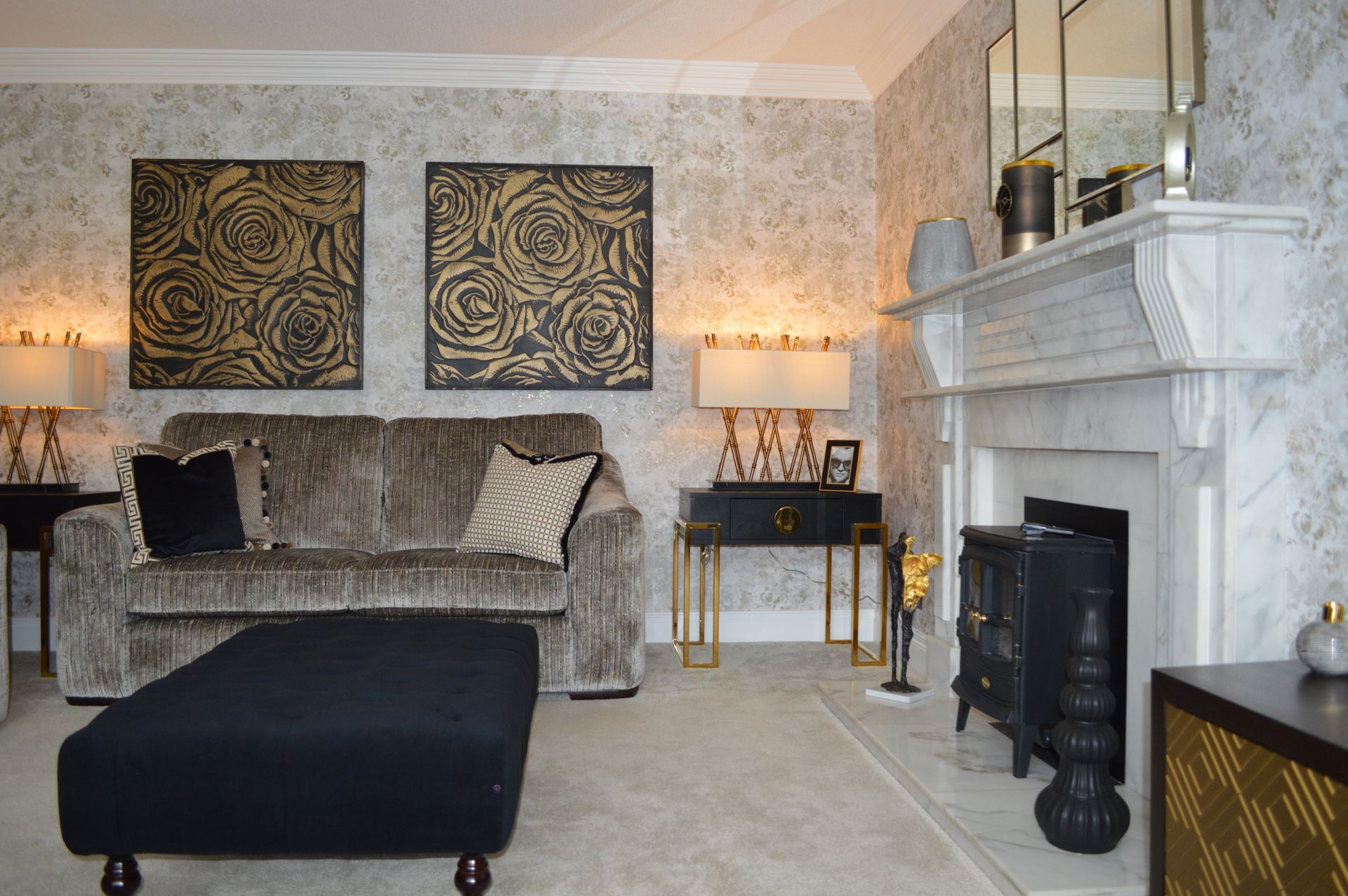 A living room with a couch , ottoman , fireplace and paintings on the wall.