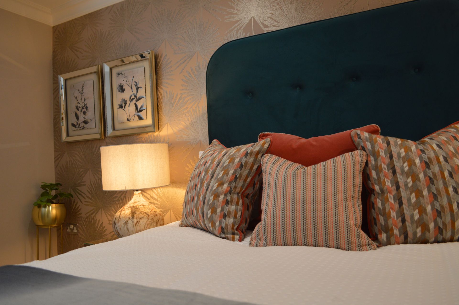 A bedroom with a bed , pillows , a lamp and paintings on the wall.