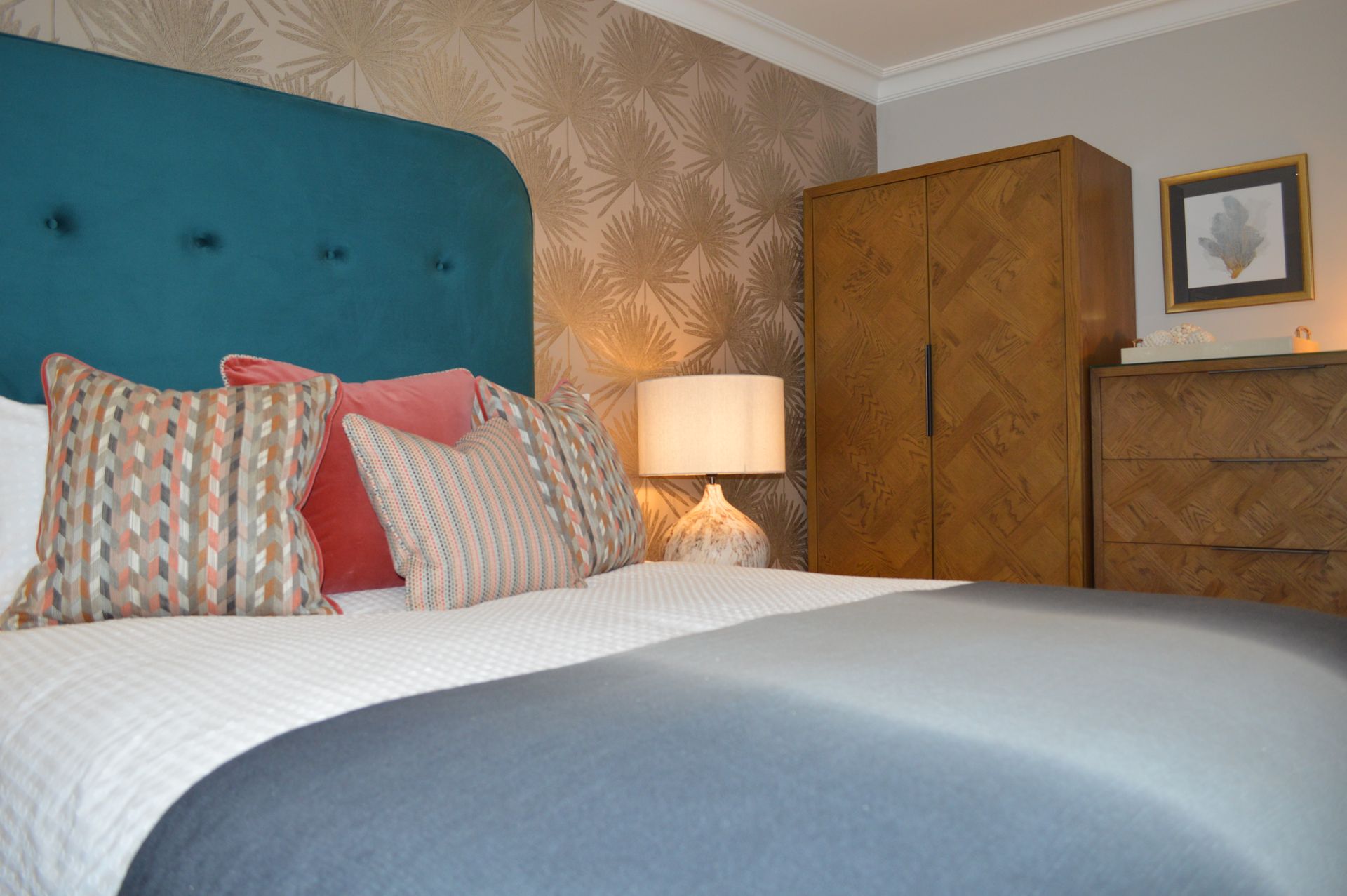 A bedroom with a bed , dresser , lamp and wardrobe.