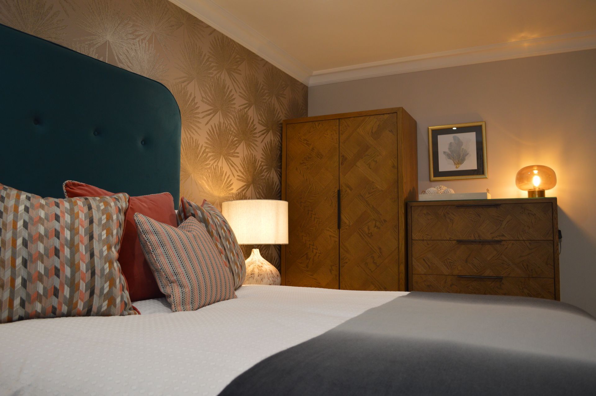 A bedroom with a bed , dresser , lamp and wardrobe.