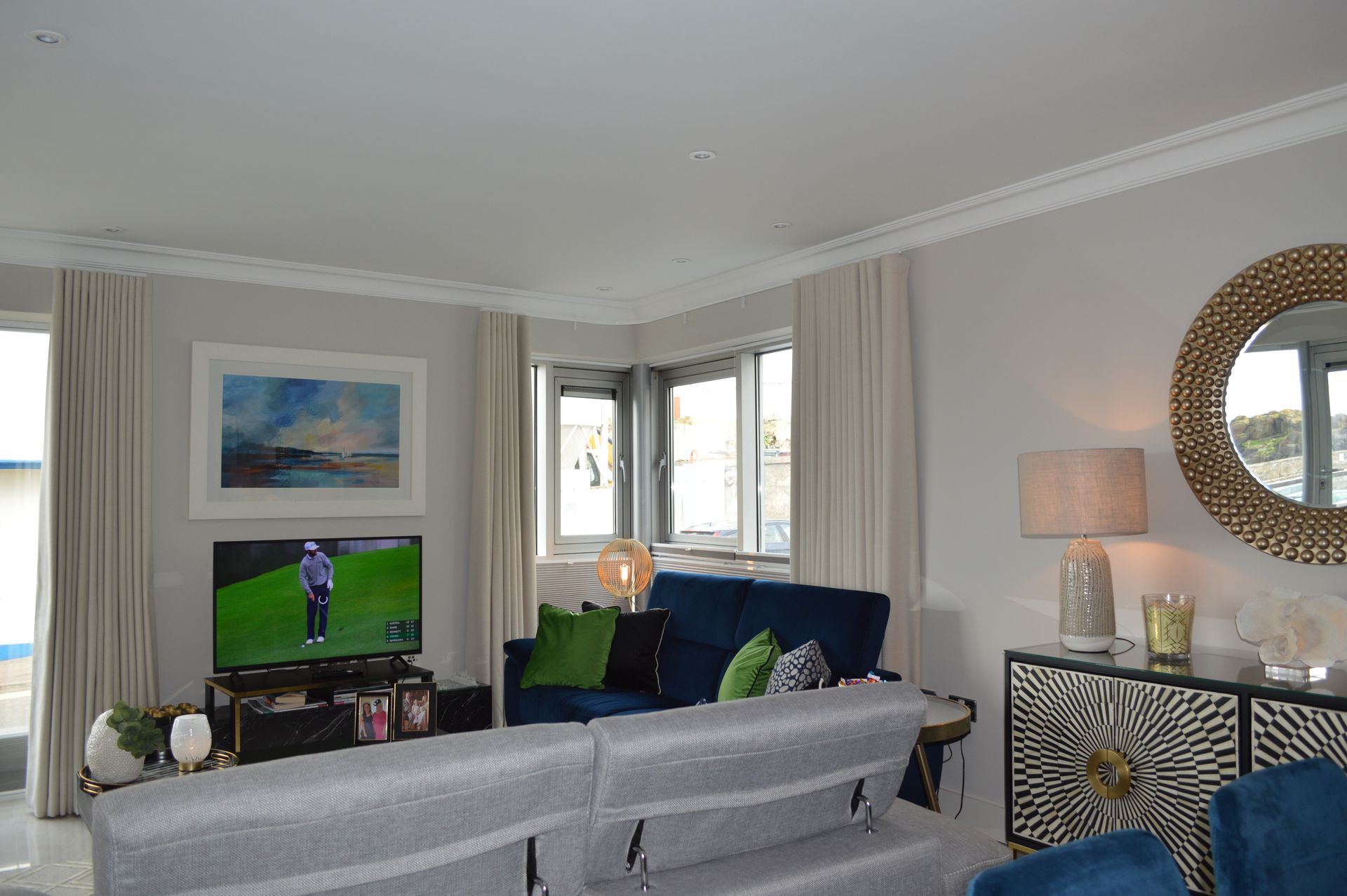 A living room with a couch , chairs , a television and a mirror.