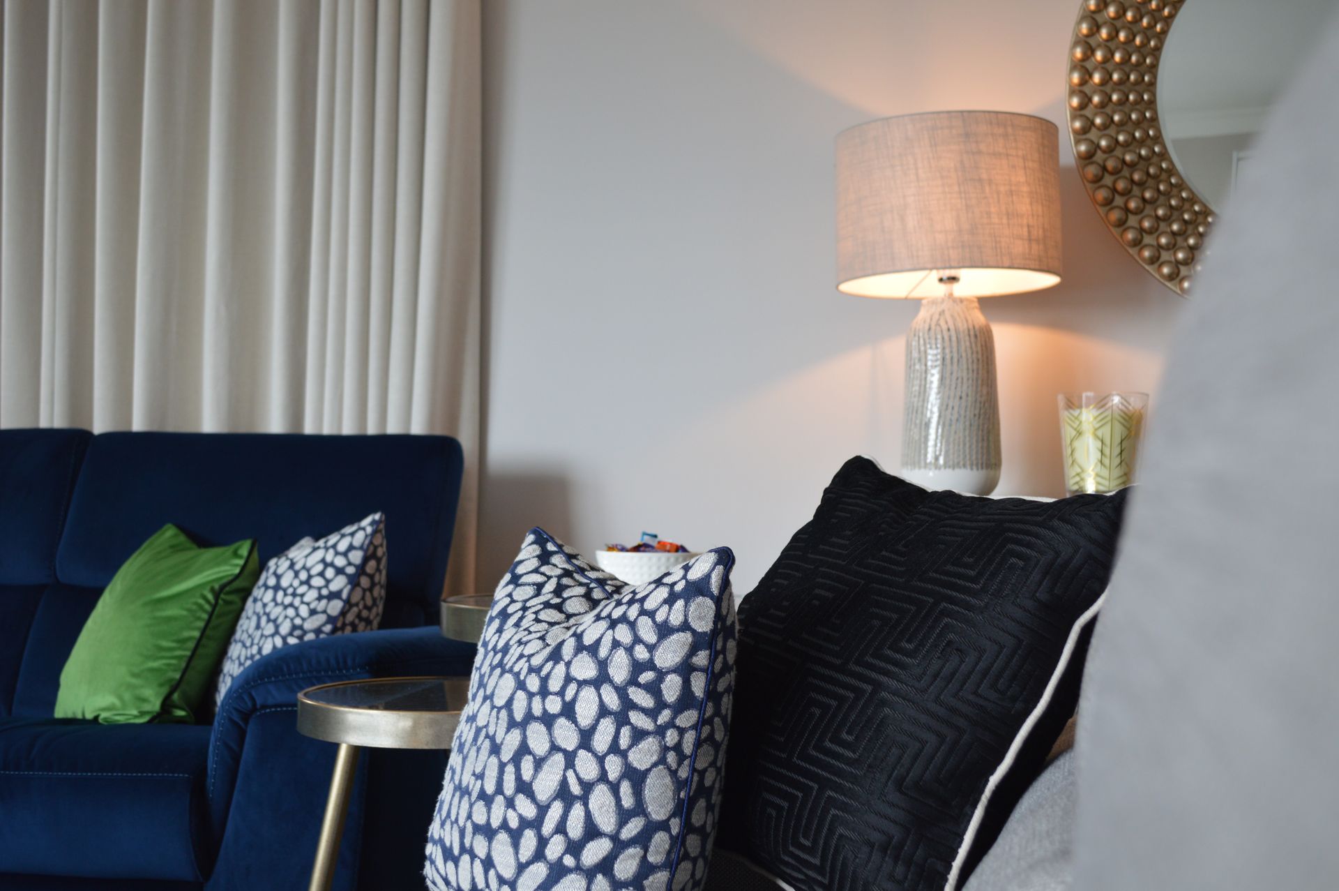 A living room with a blue couch , pillows , a lamp and a mirror.