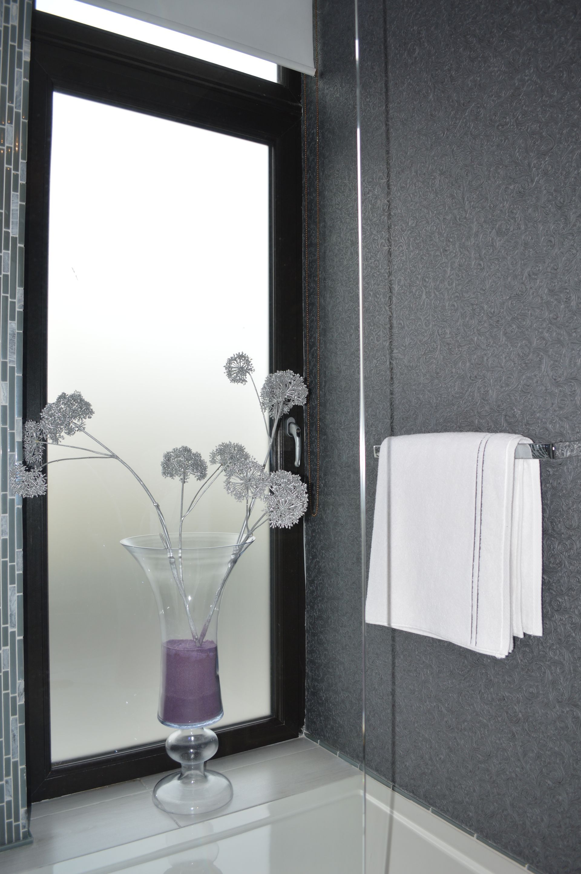 A bathroom with a window and a vase with flowers in it.