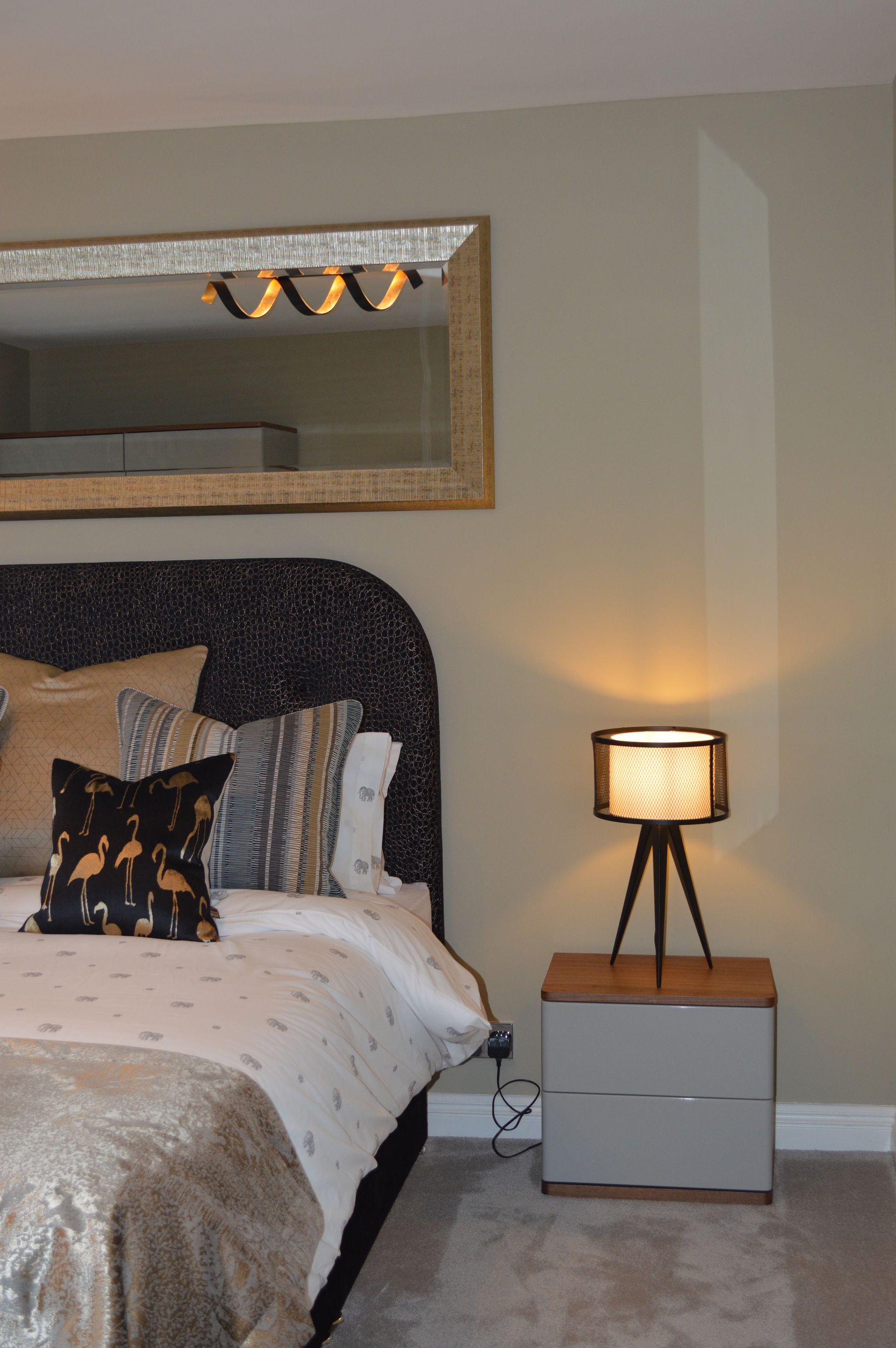 A bedroom with a bed , nightstand , lamp and mirror