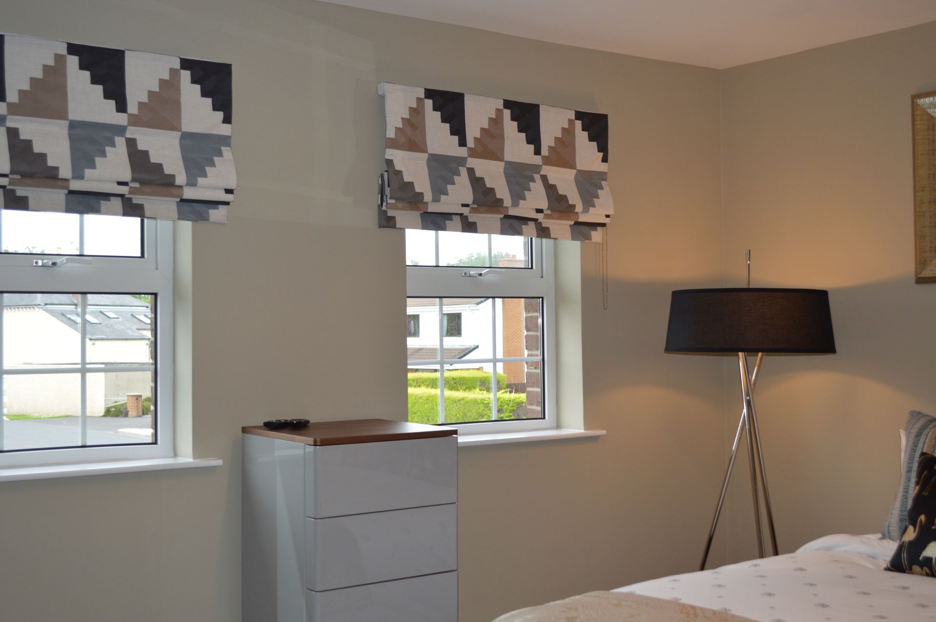 A bedroom with a bed , dresser , lamp and two windows.