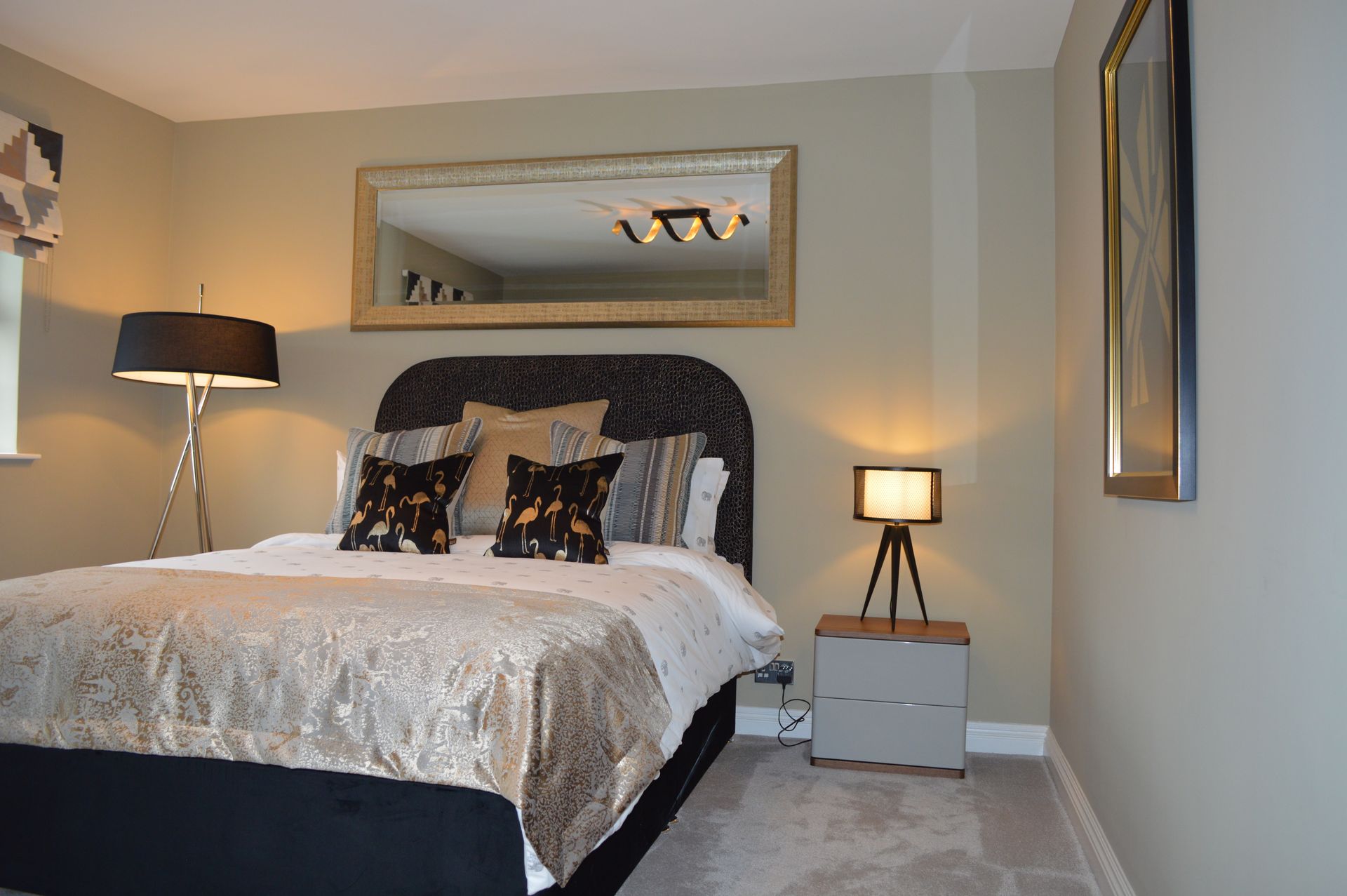 A bedroom with a bed , nightstand , lamp and mirror.