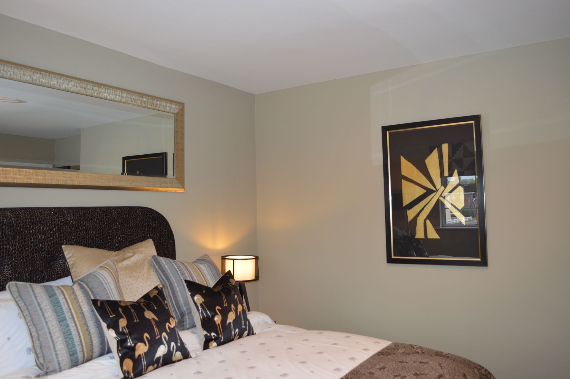 A bedroom with a bed , mirror , lamp and a picture on the wall.