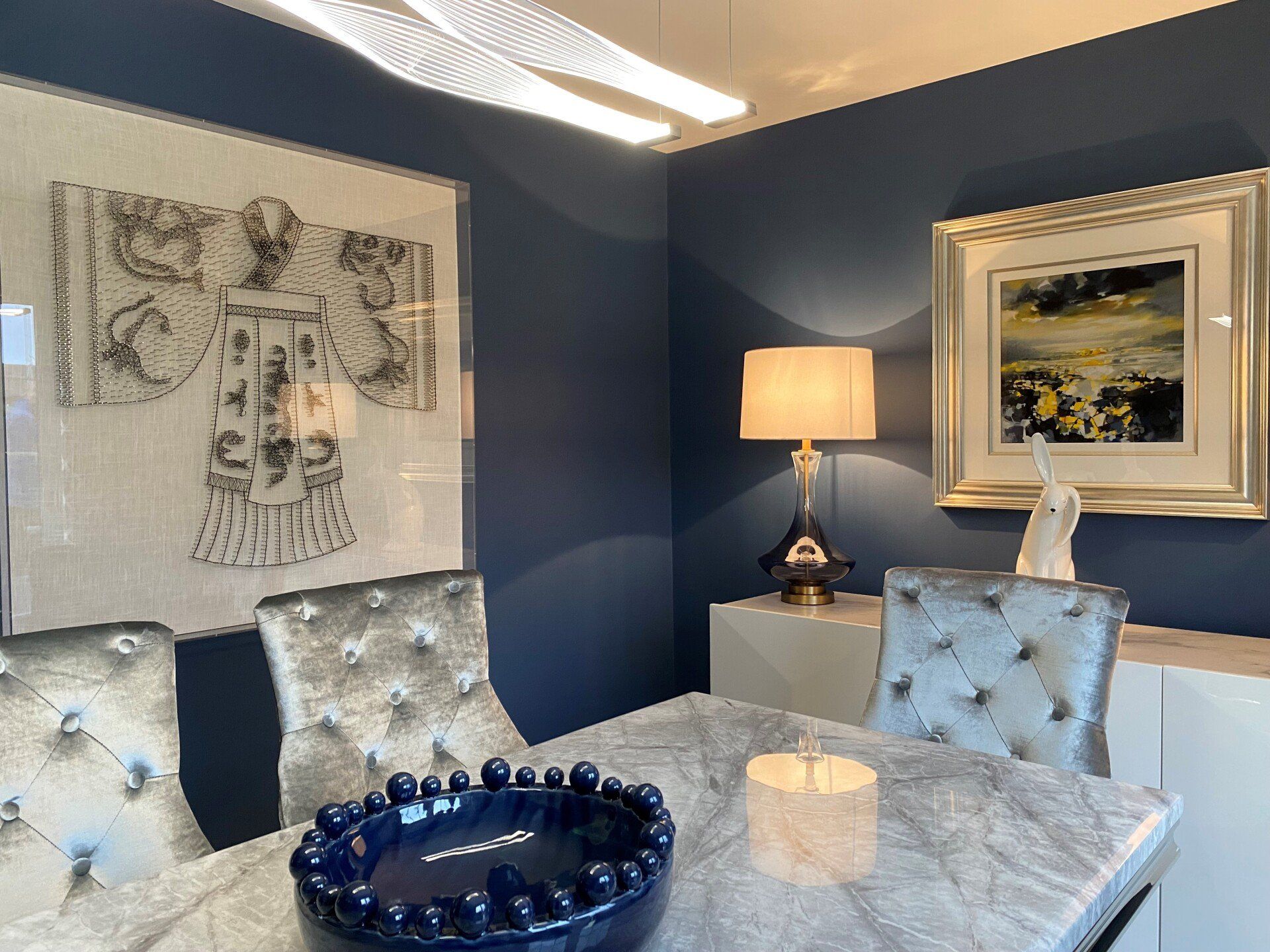A dining room with a table , chairs , a lamp and a picture on the wall.