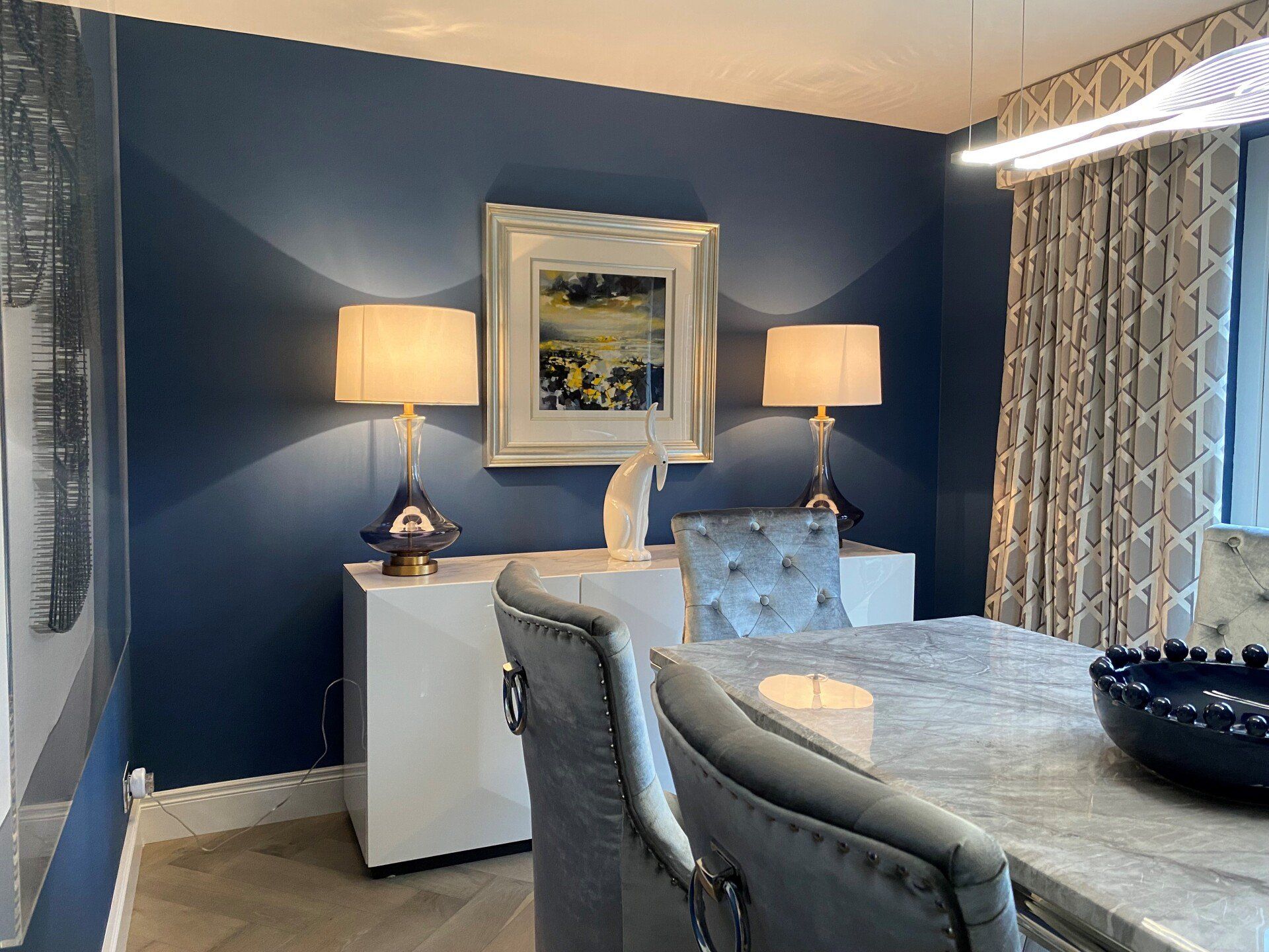 A dining room with a table , chairs , lamps and a picture on the wall.