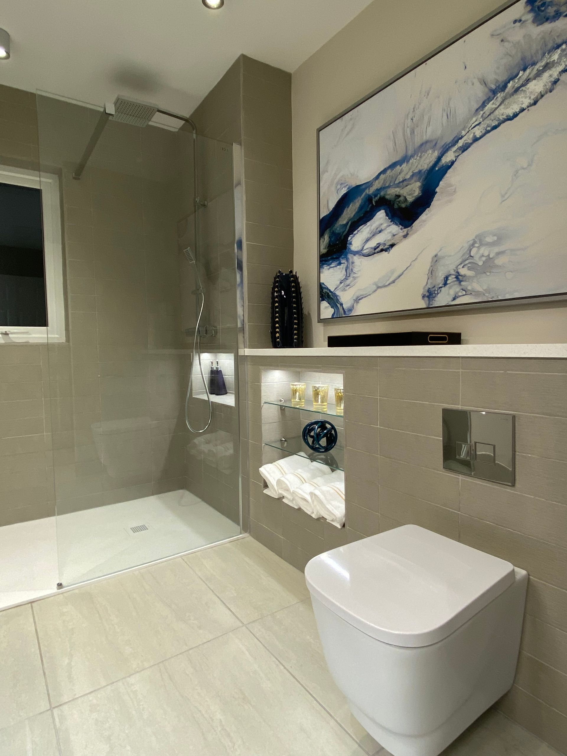 A bathroom with a toilet , shower and a painting on the wall.