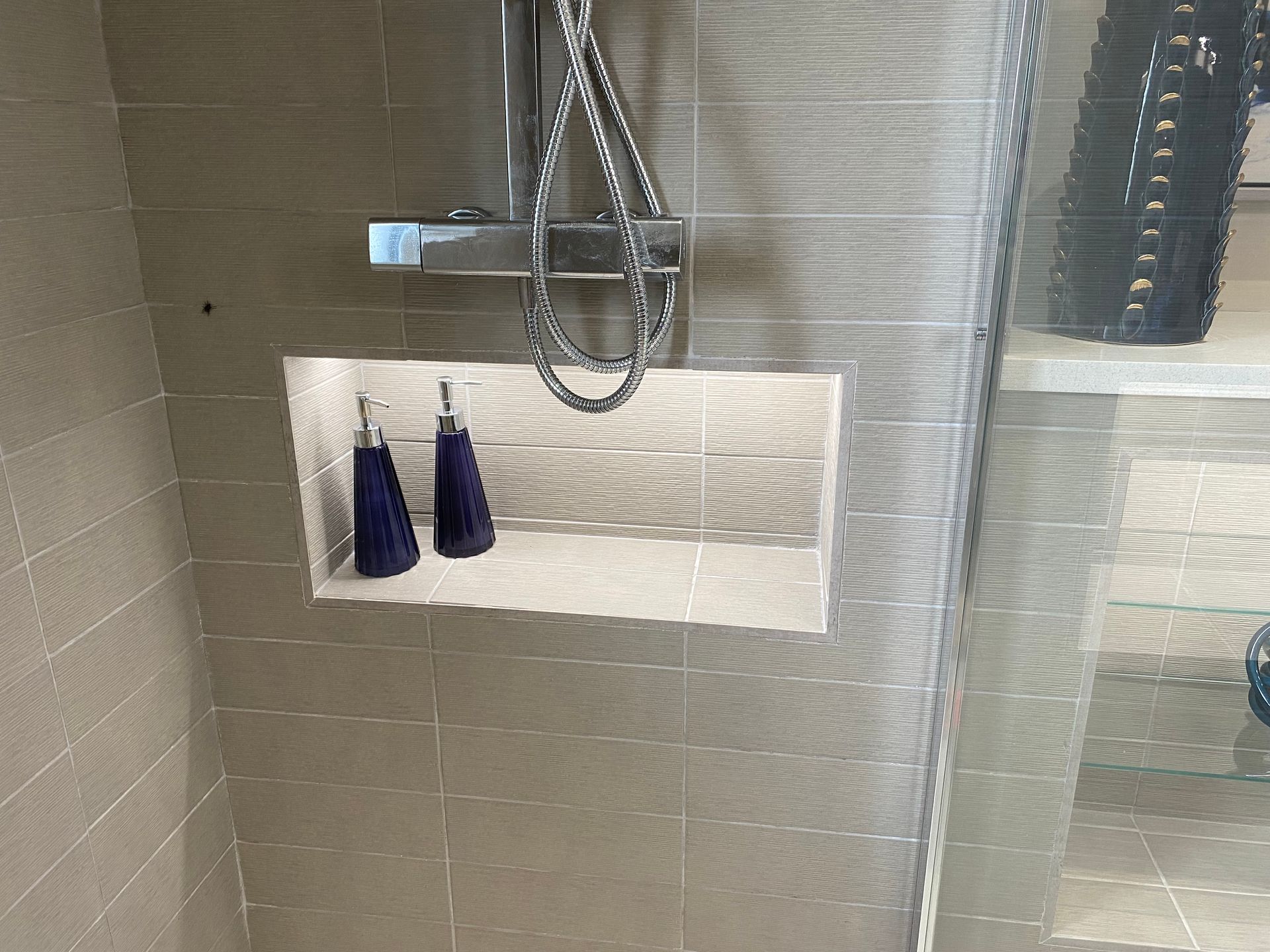 A bathroom with a shower head and a soap shelf.