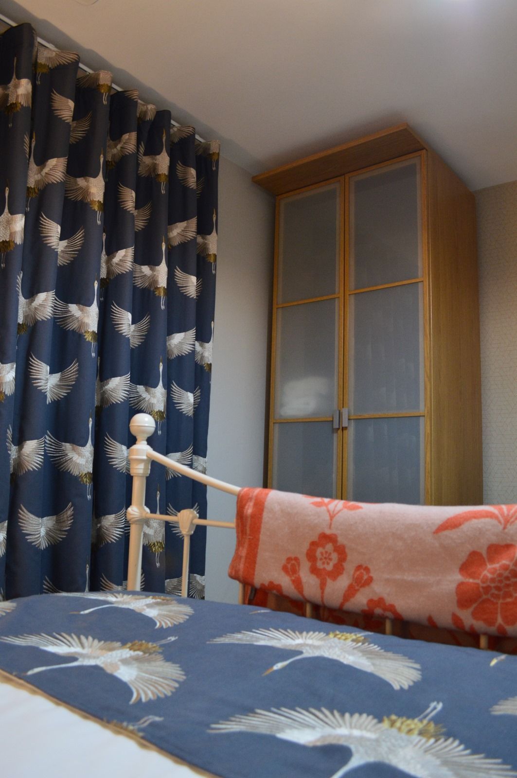 A bedroom with a bed , wardrobe and curtains with birds on them.