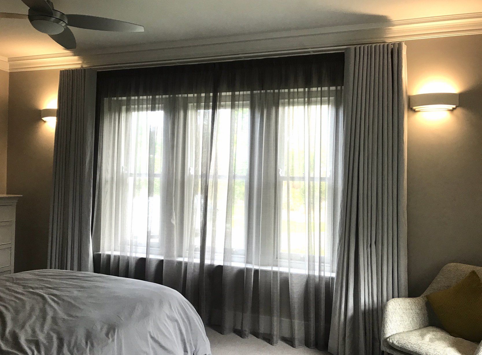 A bedroom with a bed a chair and a ceiling fan