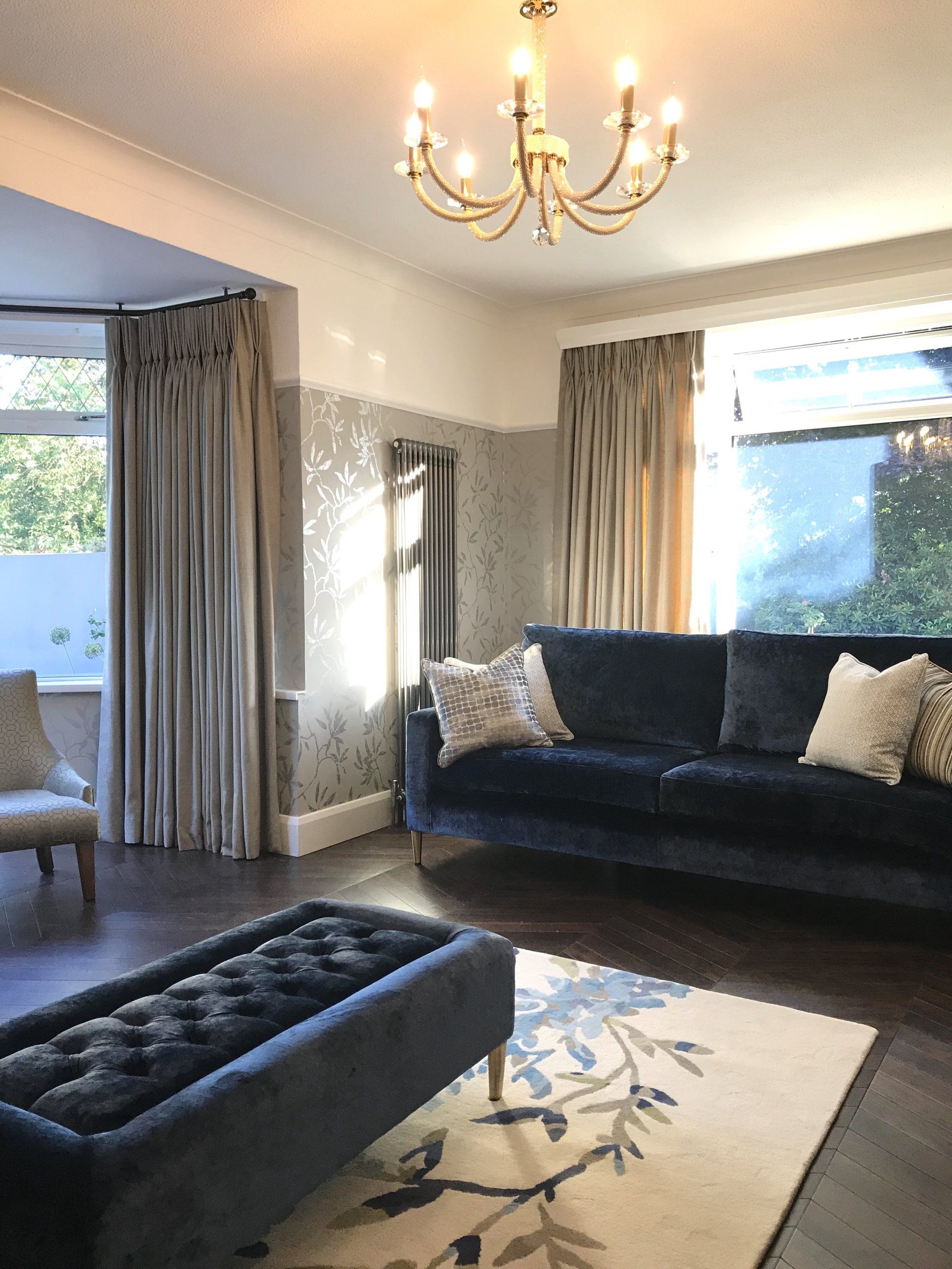 A living room with a couch , chair , rug and chandelier.