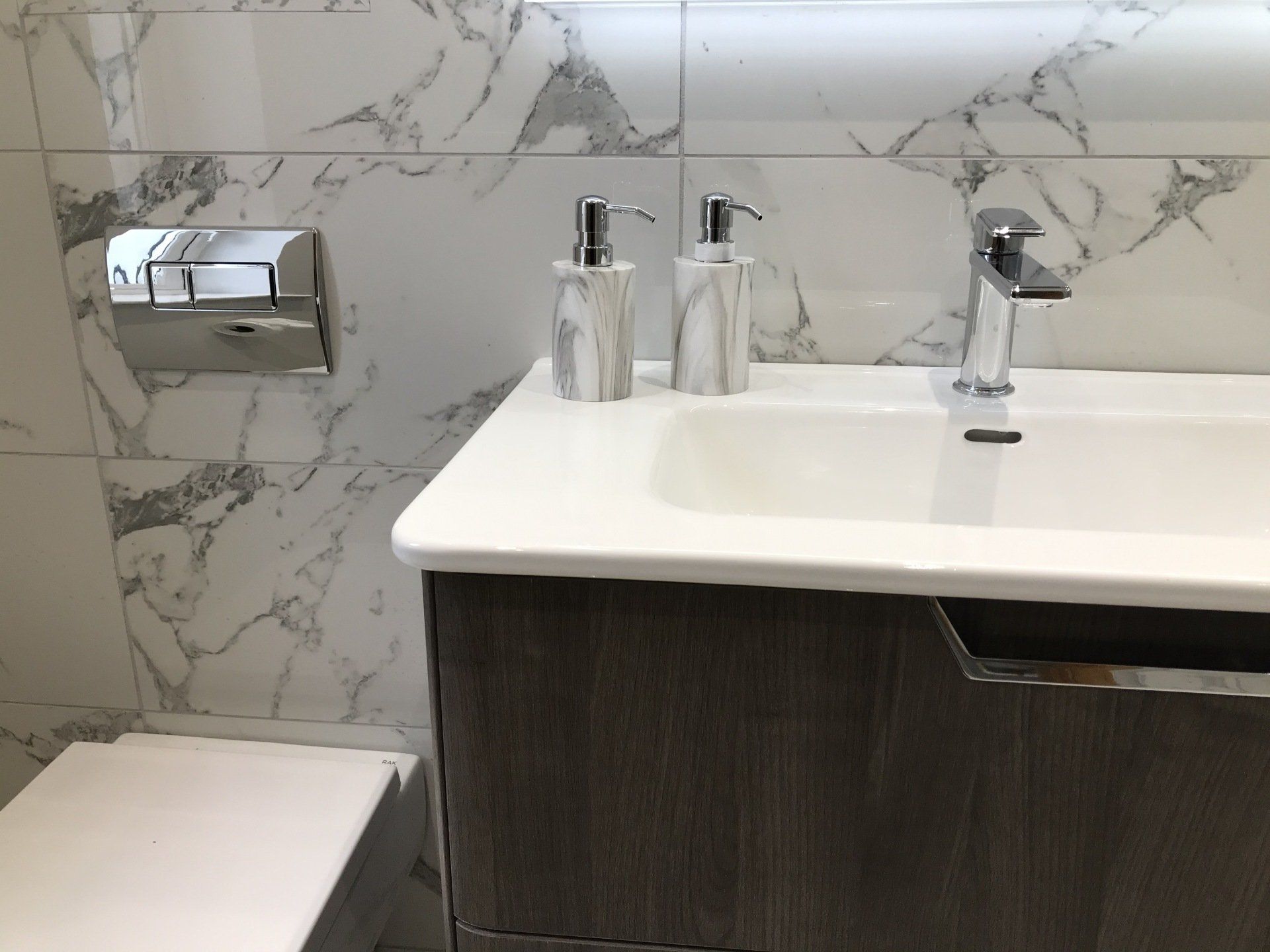 A bathroom with a sink , toilet and soap dispensers.