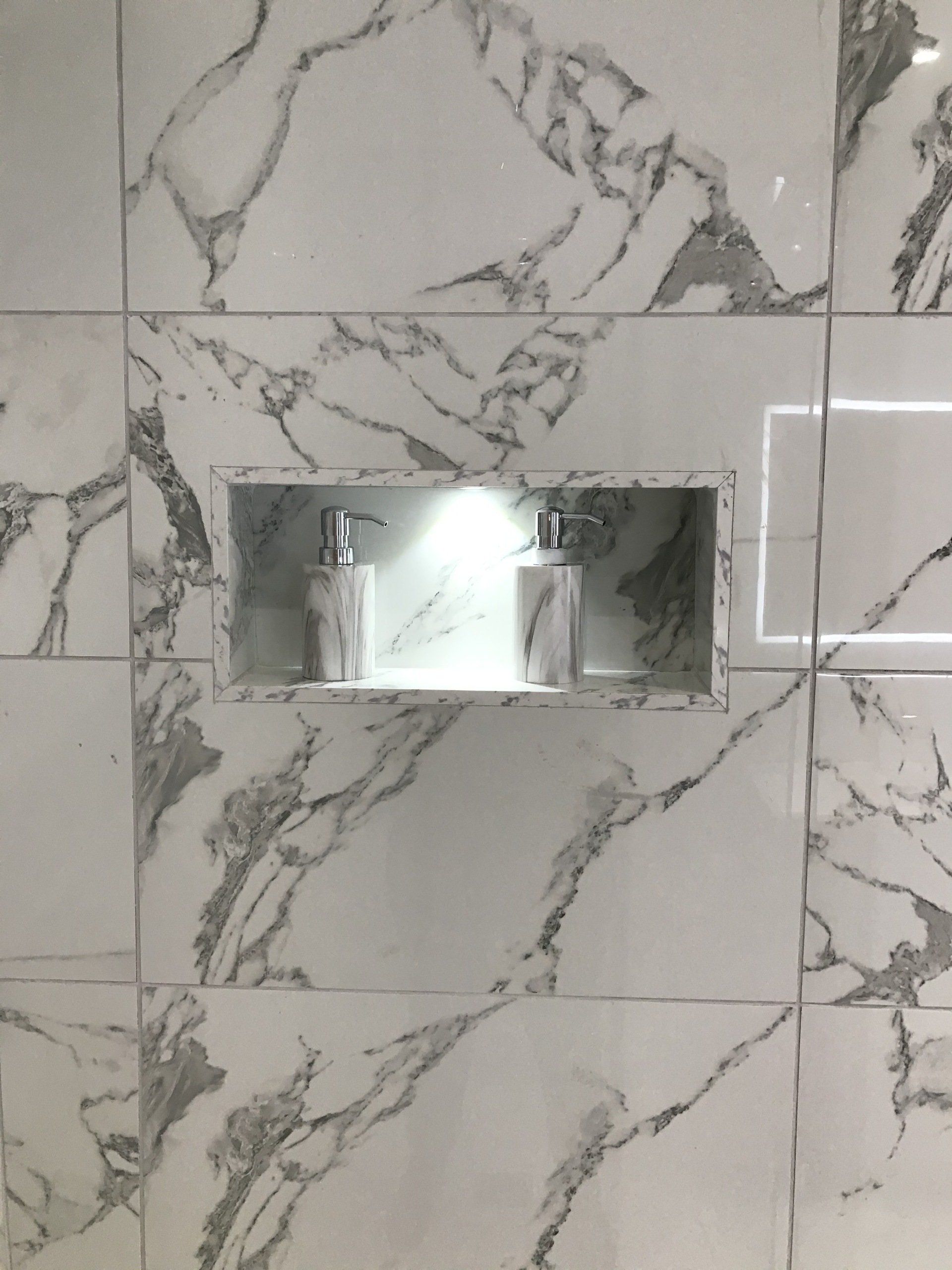 A bathroom with marble tiles and a soap dispenser in a niche.