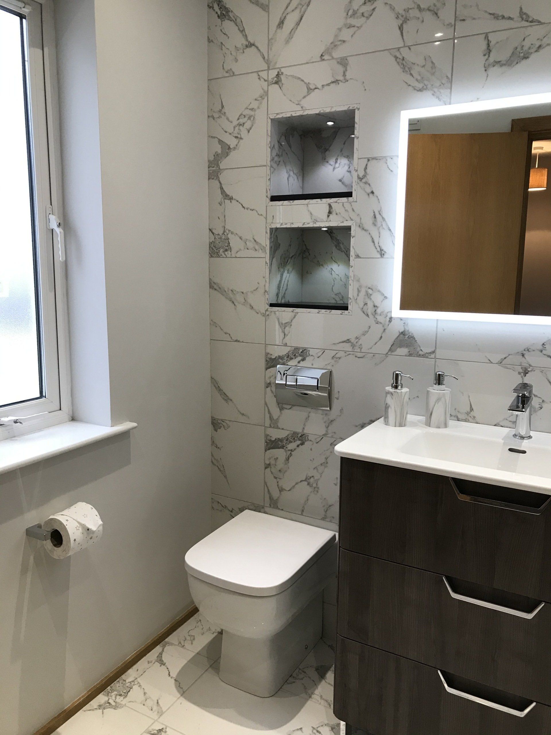 A bathroom with a toilet , sink , mirror and window.