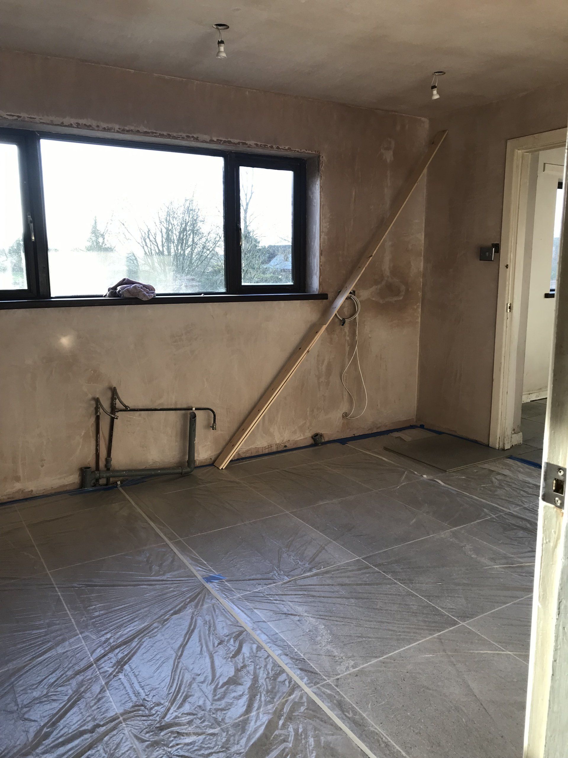 An empty room with a plastic sheet on the floor and a window.