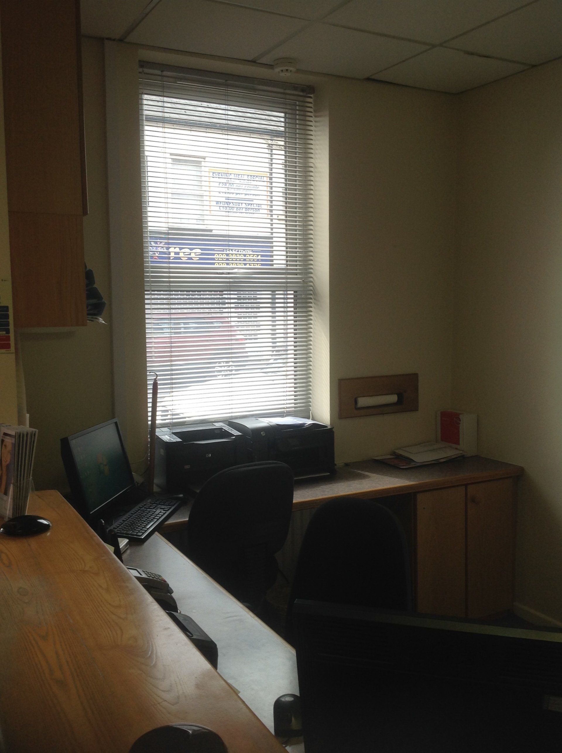 A desk with a laptop and a printer in front of a window with blinds