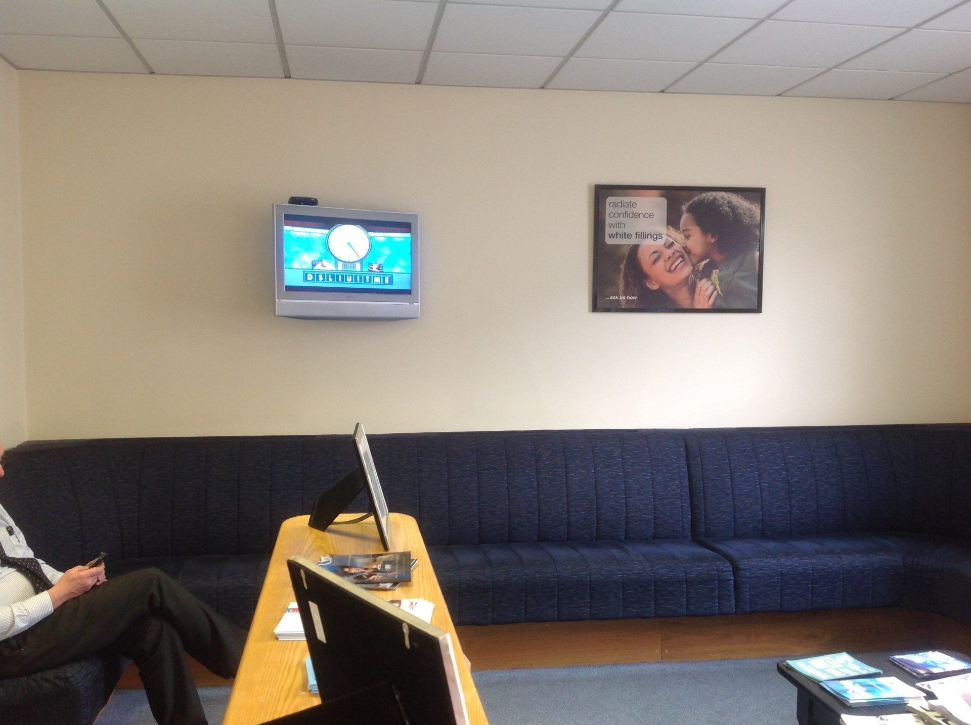 Two people sit in a waiting room with a picture of a man and woman on the wall above them