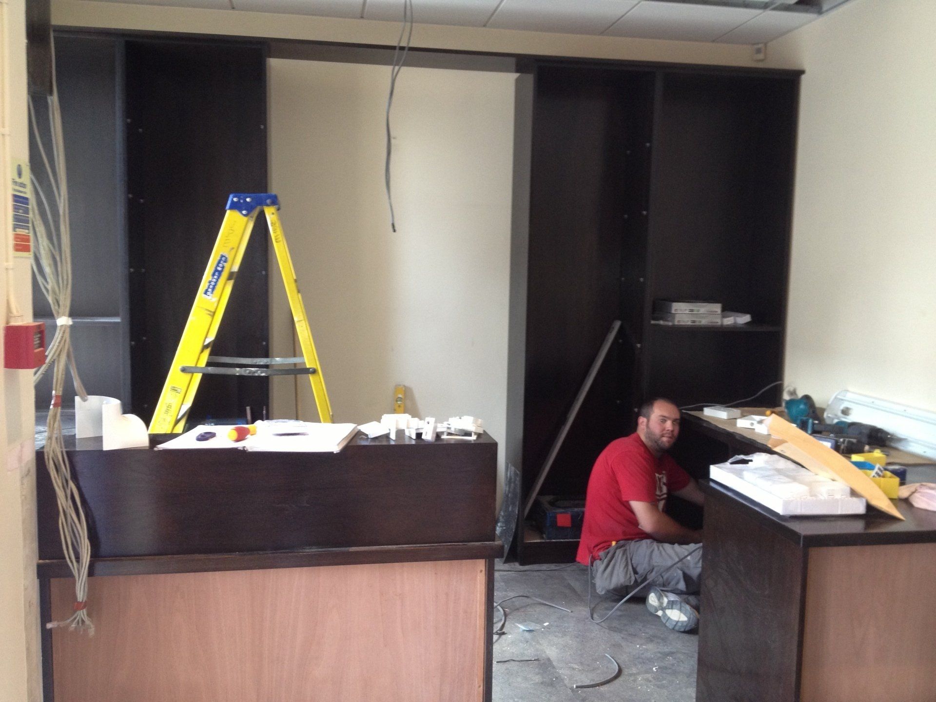 A man in a red shirt is working in a room with a yellow ladder