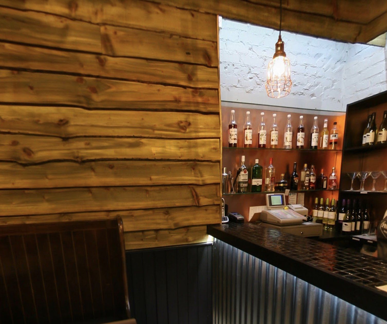 A bar with a wooden wall and bottles on shelves
