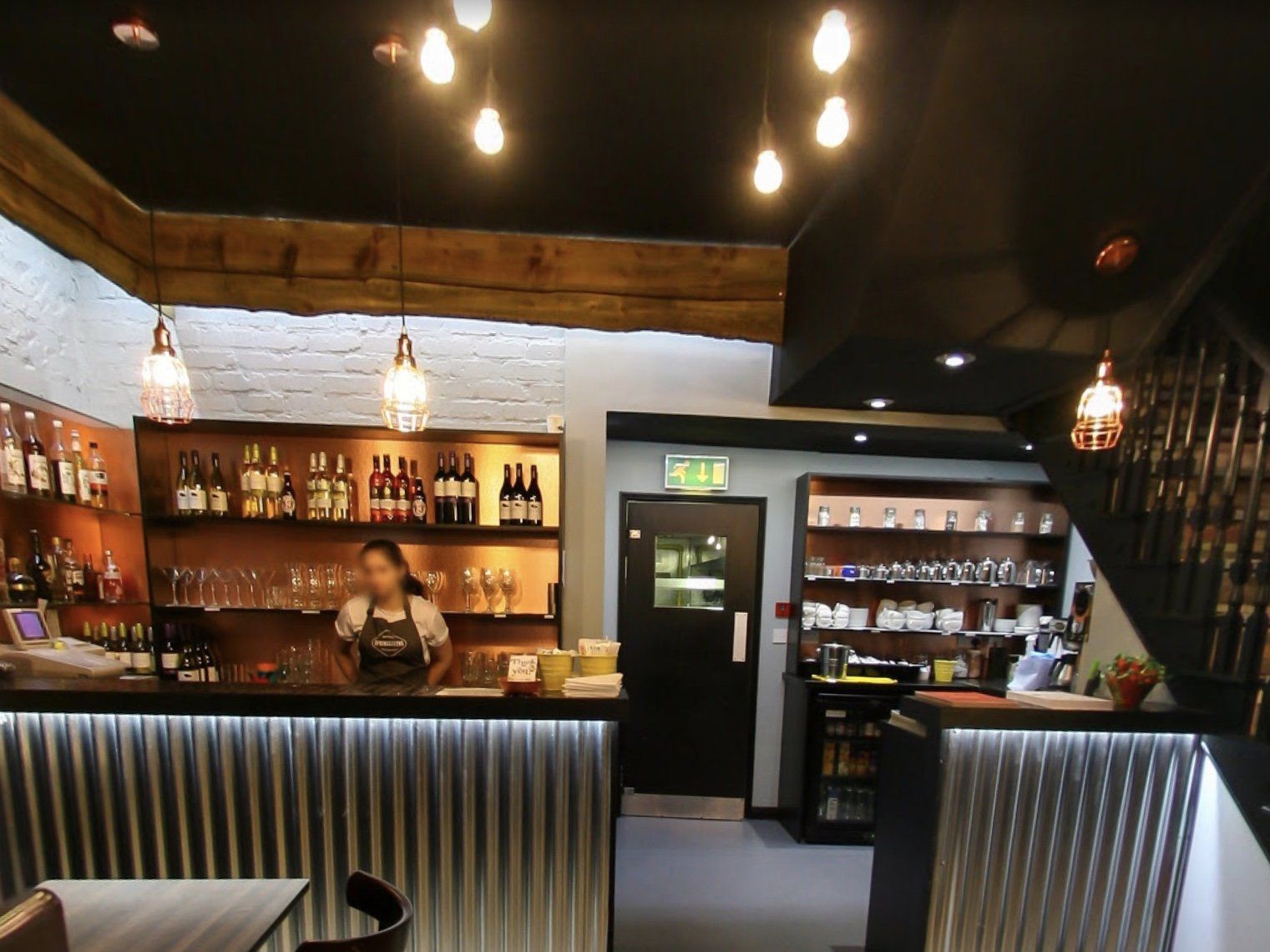 A woman in an apron stands behind a bar in a restaurant