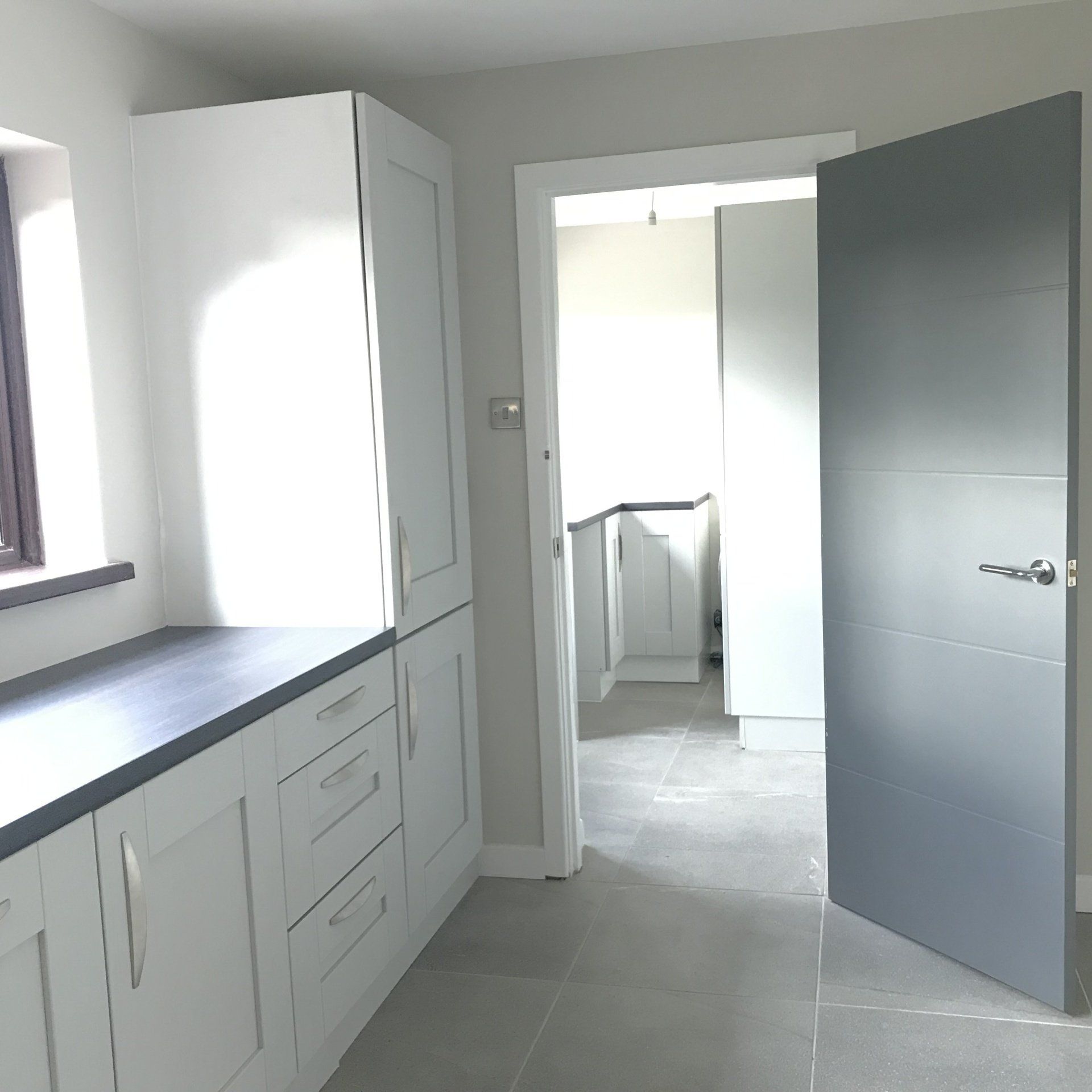 A kitchen with white cabinets and a gray door
