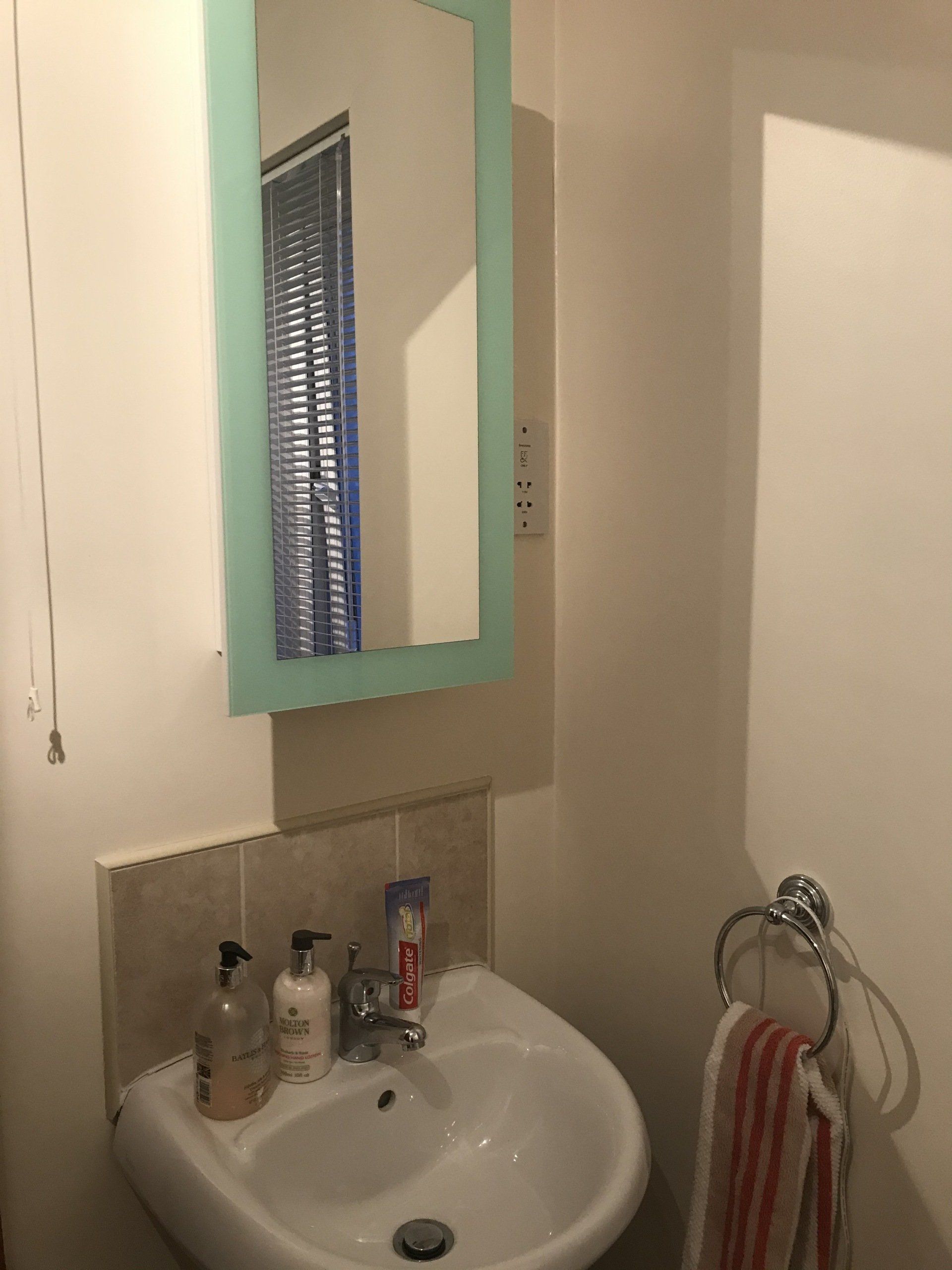 A bathroom with a sink , mirror and towel rack.