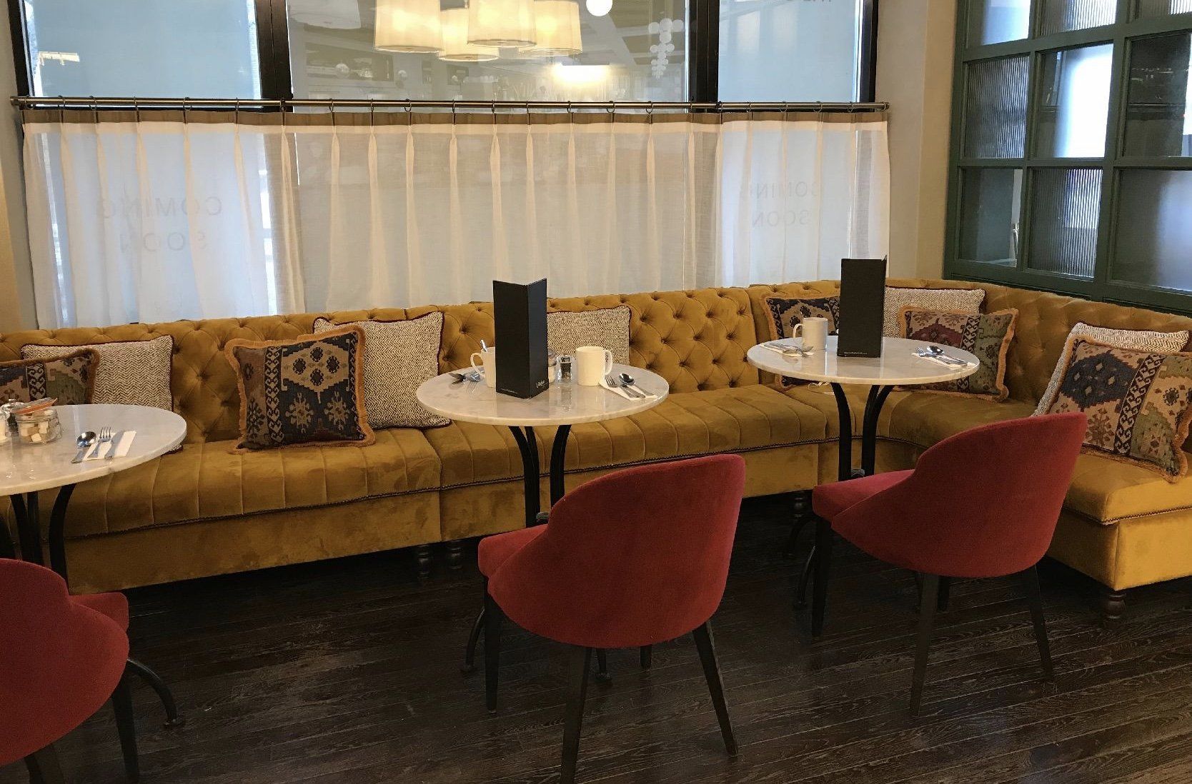 A restaurant with a yellow couch and red chairs and tables.