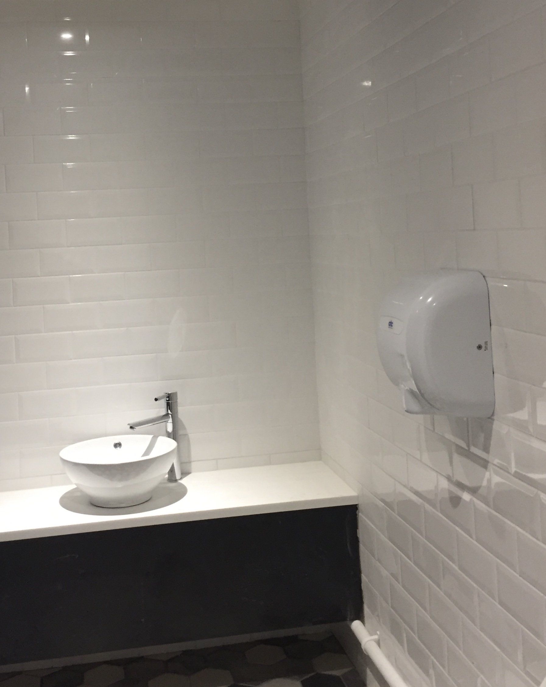 A bathroom with white tiles , a sink , and a toilet.