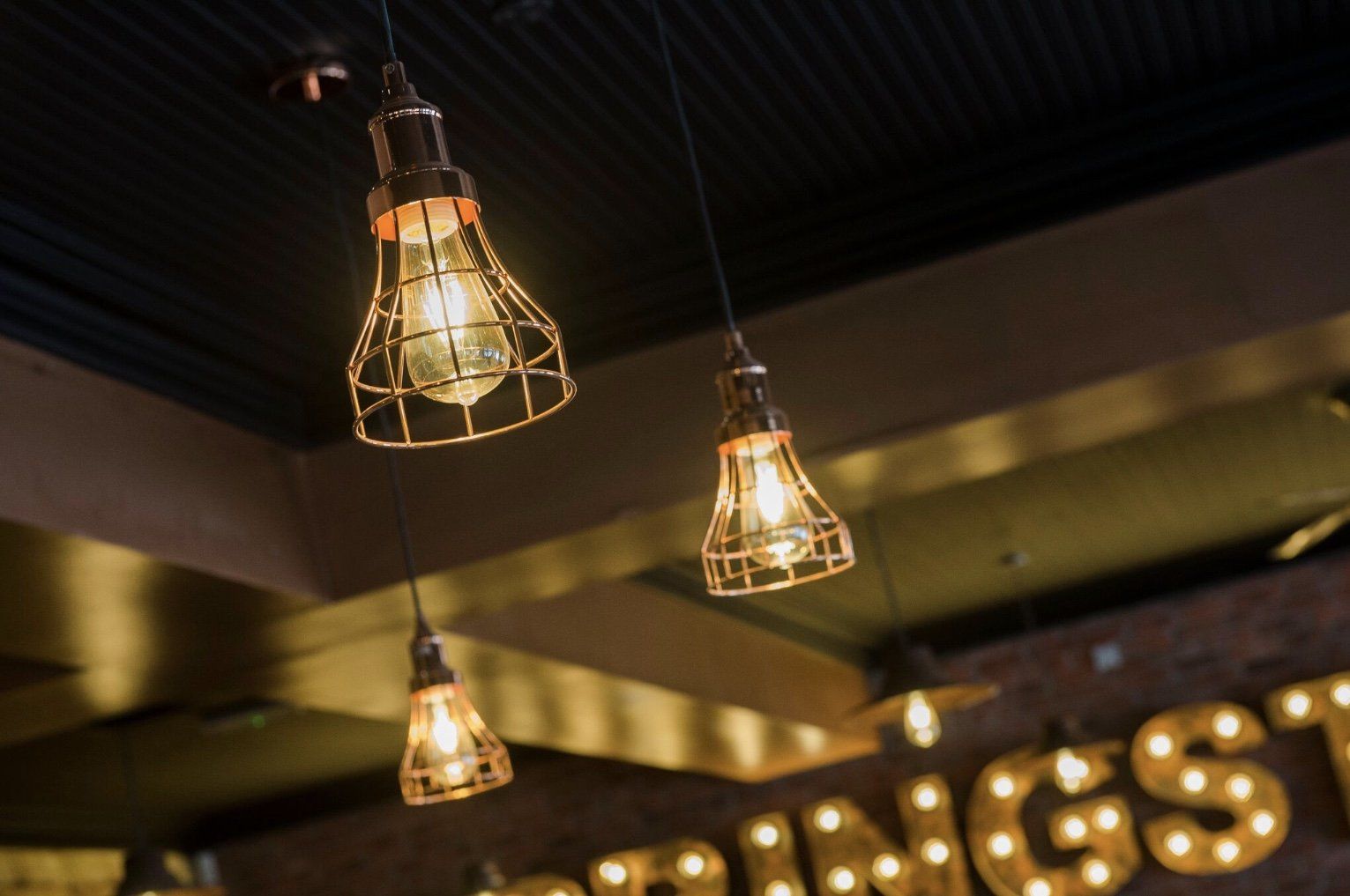 Three light bulbs are hanging from the ceiling in front of a sign that says wings