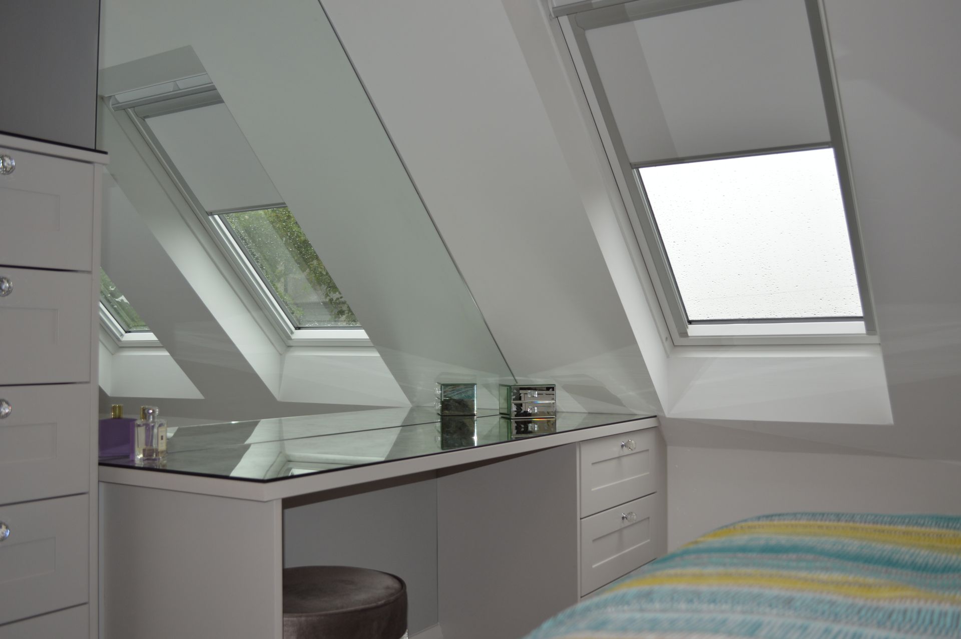 A bedroom with a bed , dresser , desk and skylights.