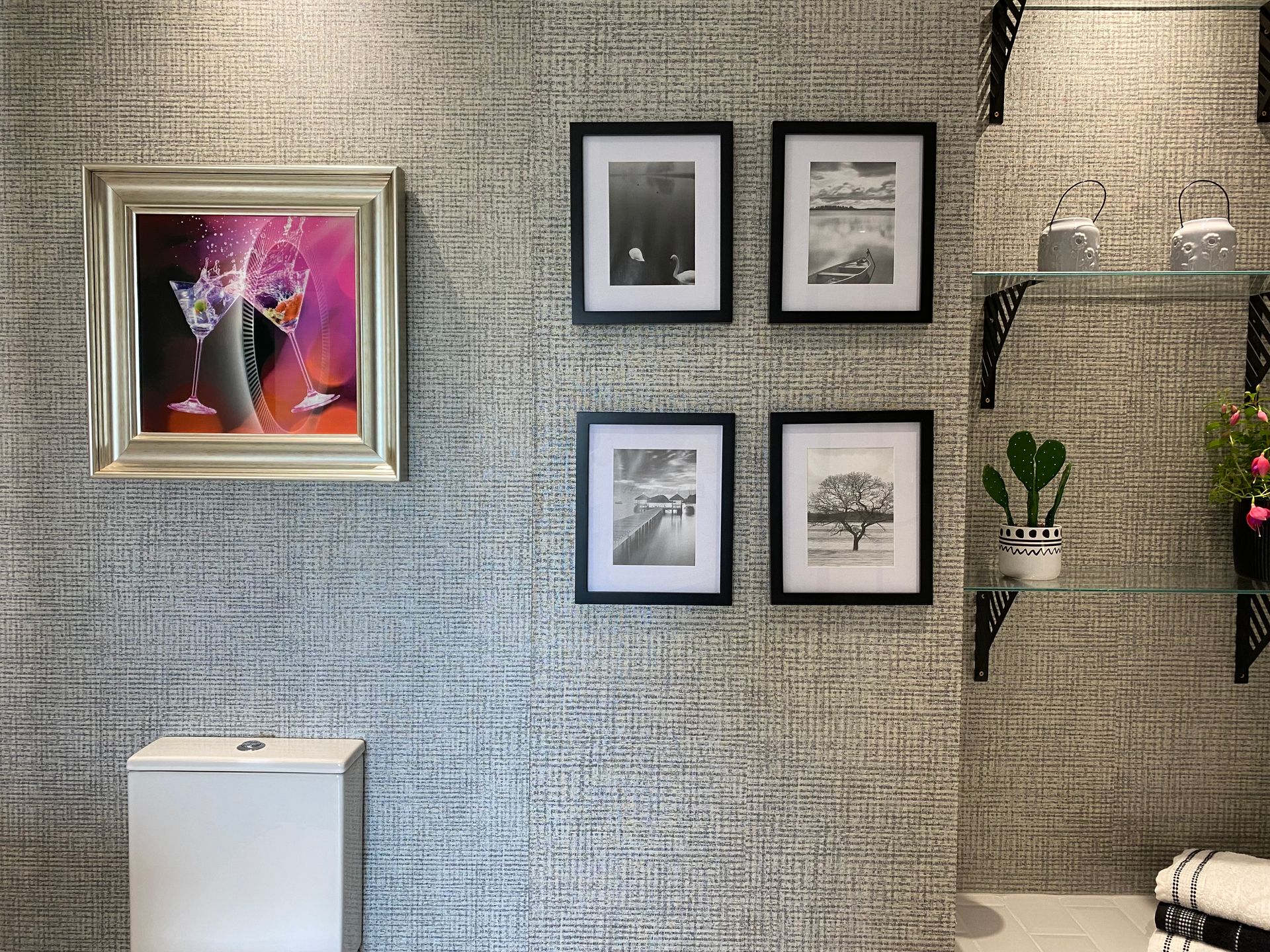 A bathroom with a painting on the wall and pictures on the shelves.