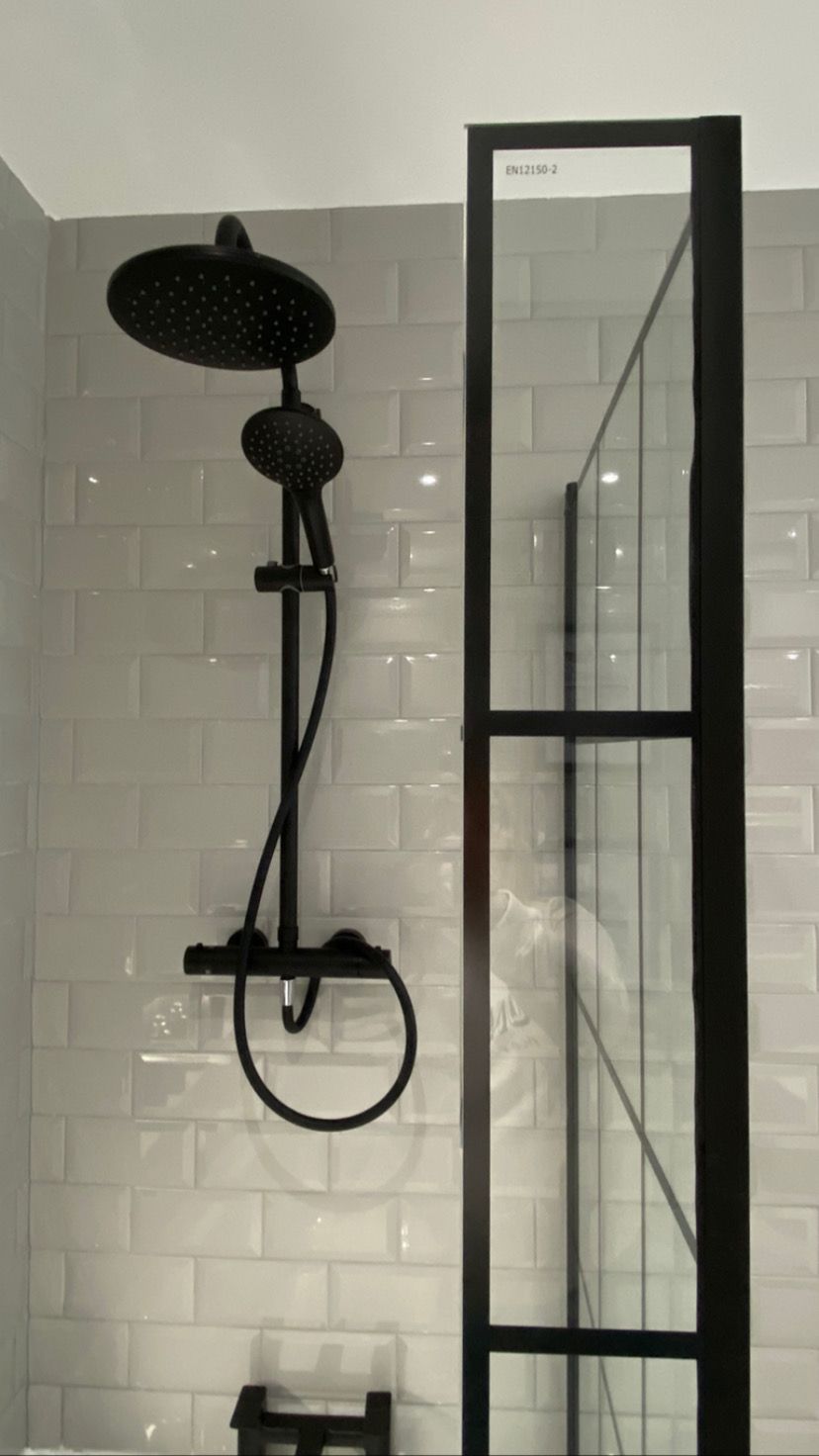 A black shower head is hanging from the ceiling in a bathroom with white tiles.