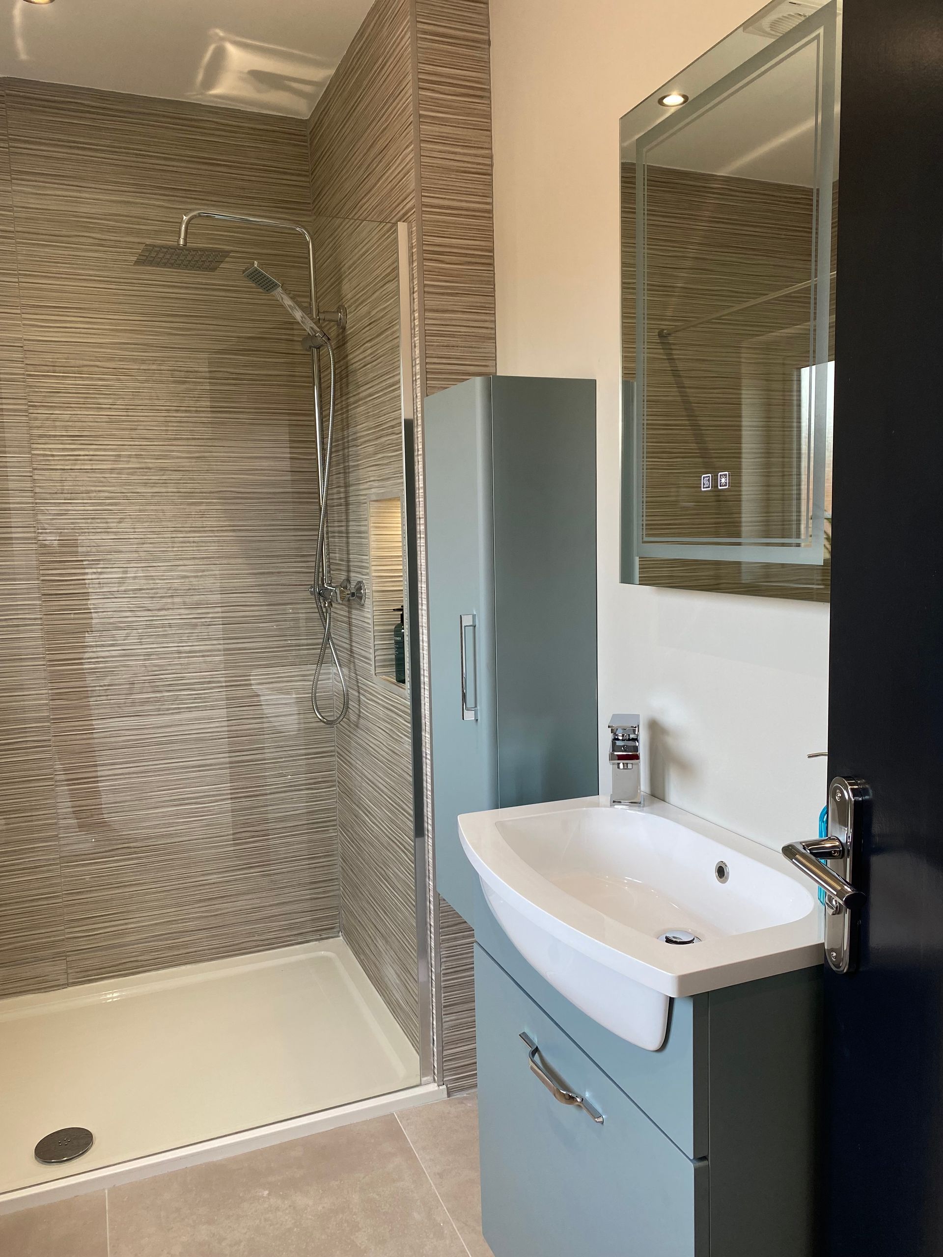 A bathroom with a sink , mirror and walk in shower.