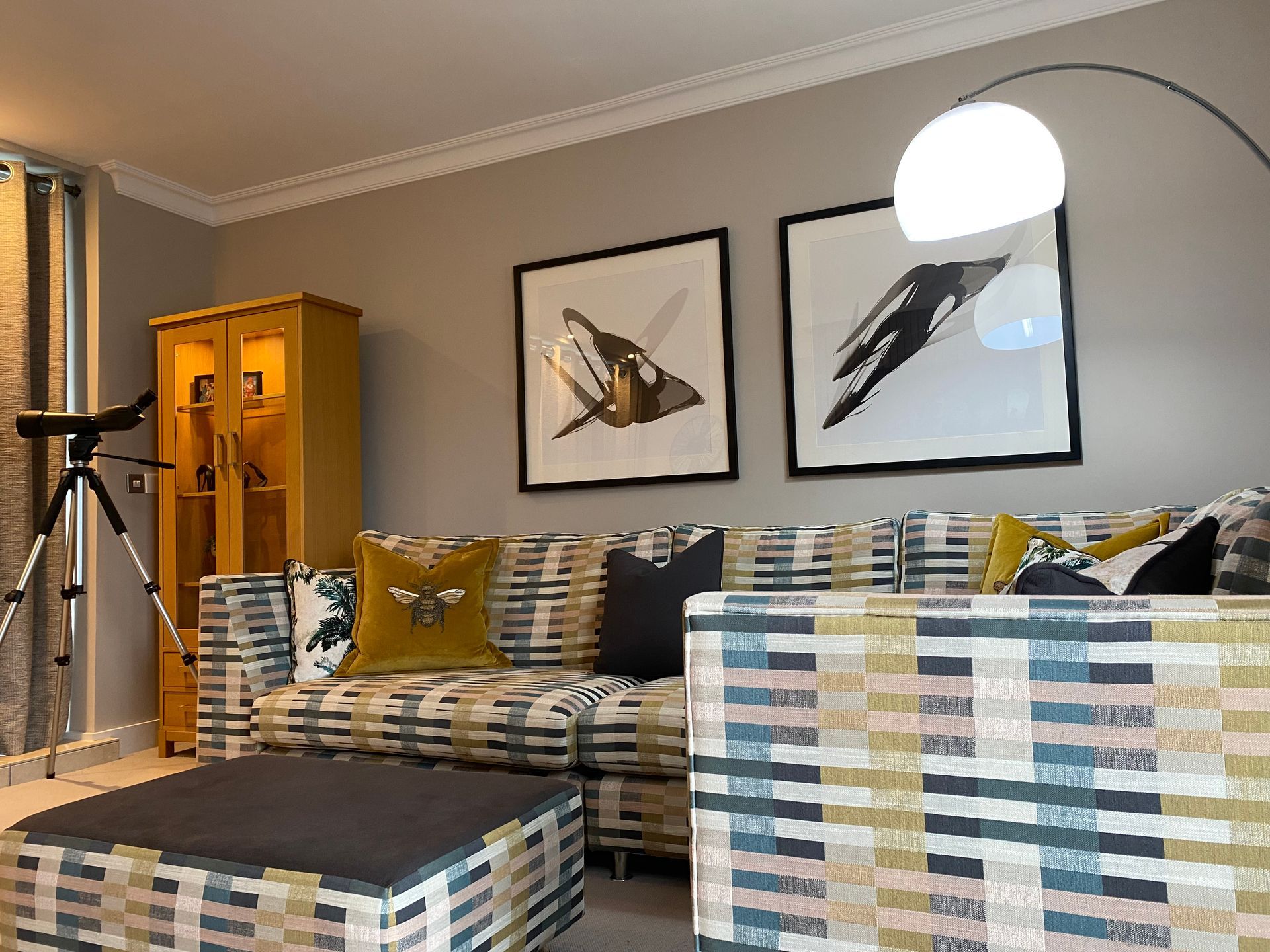 A living room with a couch , chair , ottoman , lamp and paintings on the wall.