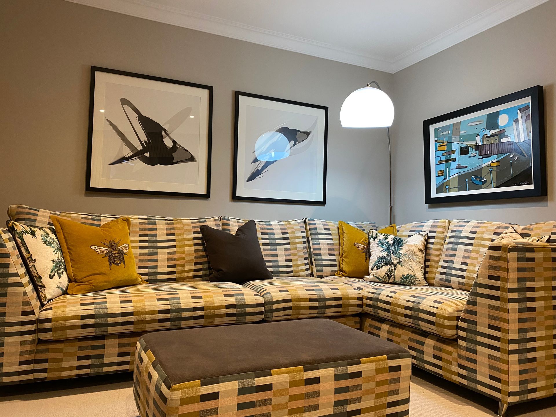 A living room with a couch , ottoman , and paintings on the wall.