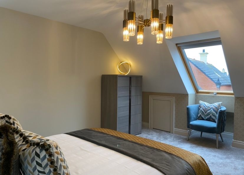 A bedroom with a bed , chair , dresser and window.