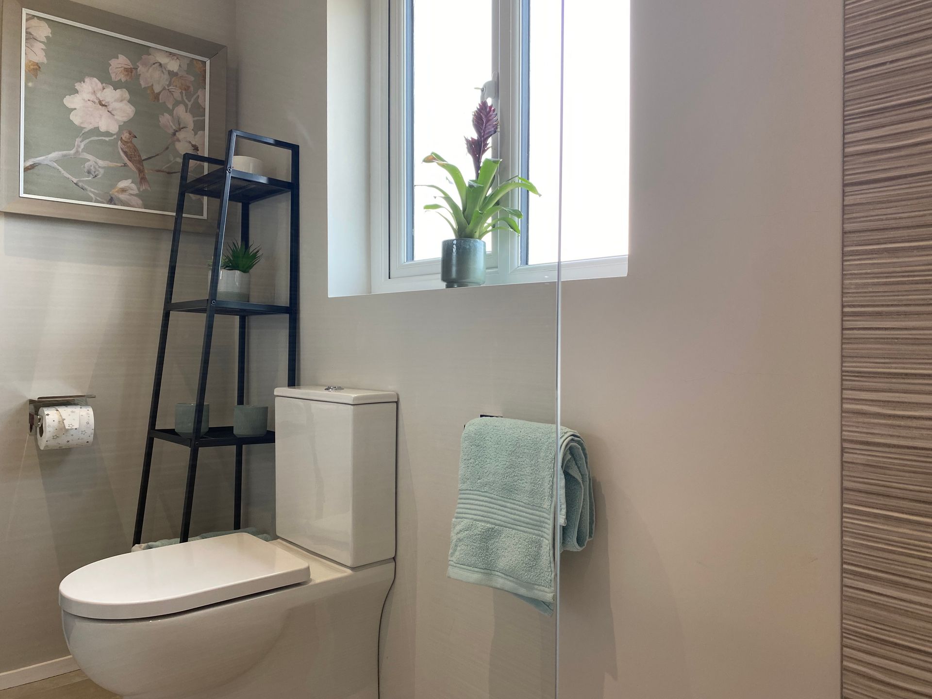 A bathroom with a toilet , shelves , and a window.