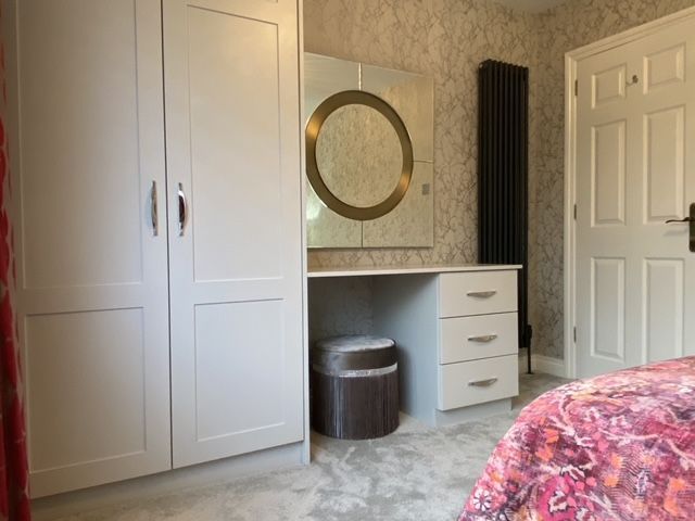 A bedroom with a bed , dresser , mirror and wardrobe.