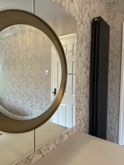 A bathroom with a round mirror and a black radiator