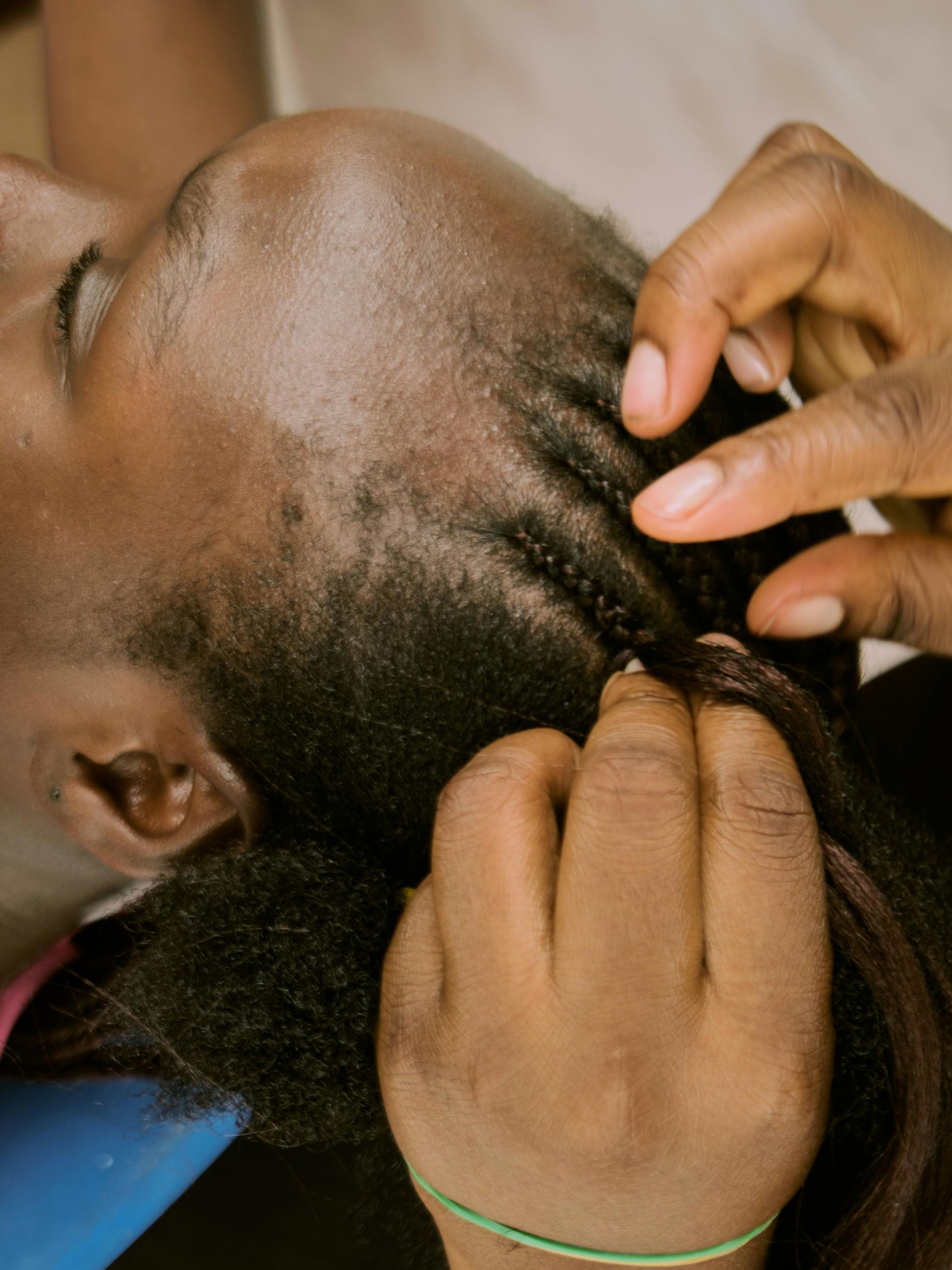 Hands braiding hair on a person's head. Dark skin, small braids being created.