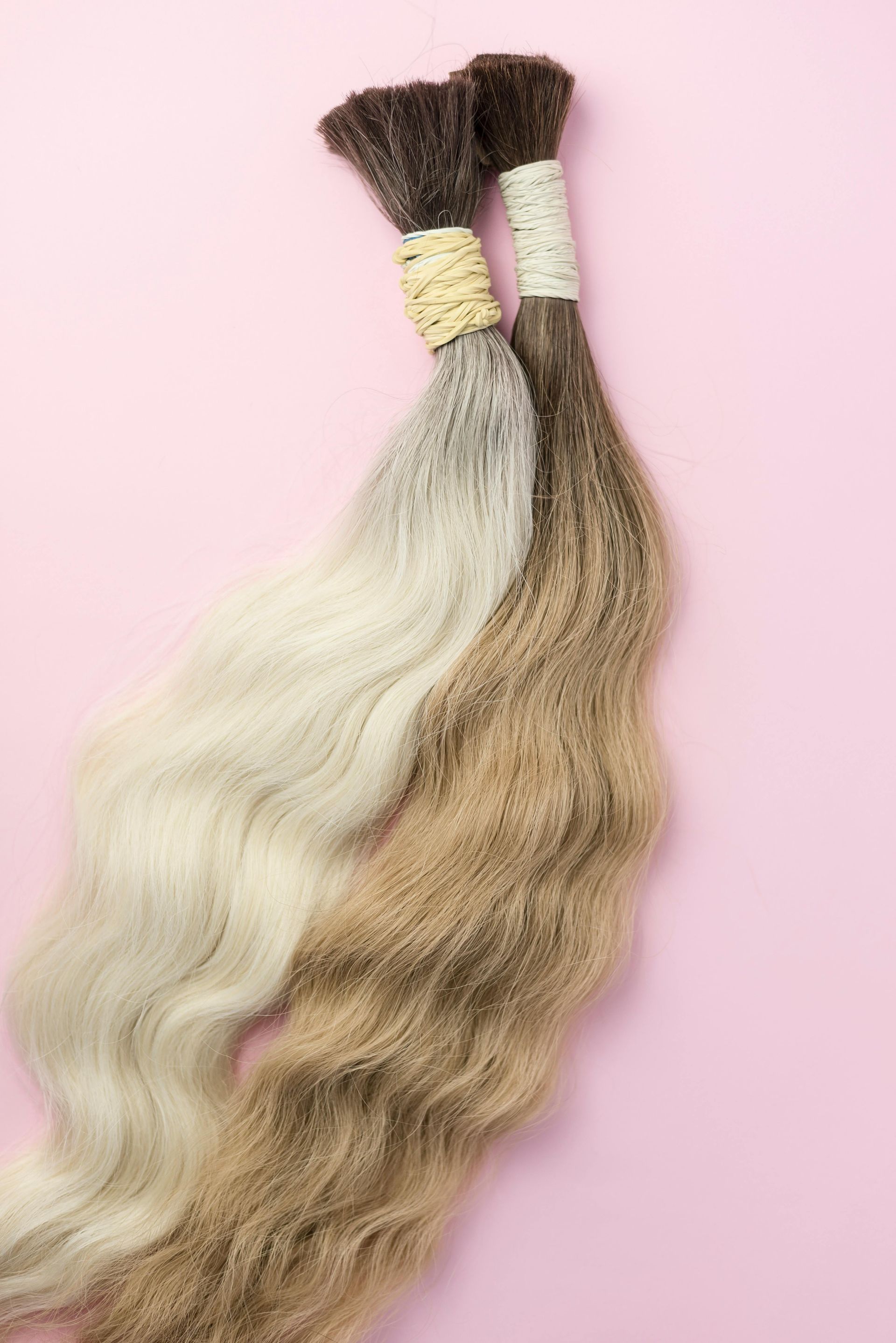 Two bundles of ombre hair extensions on pink background.