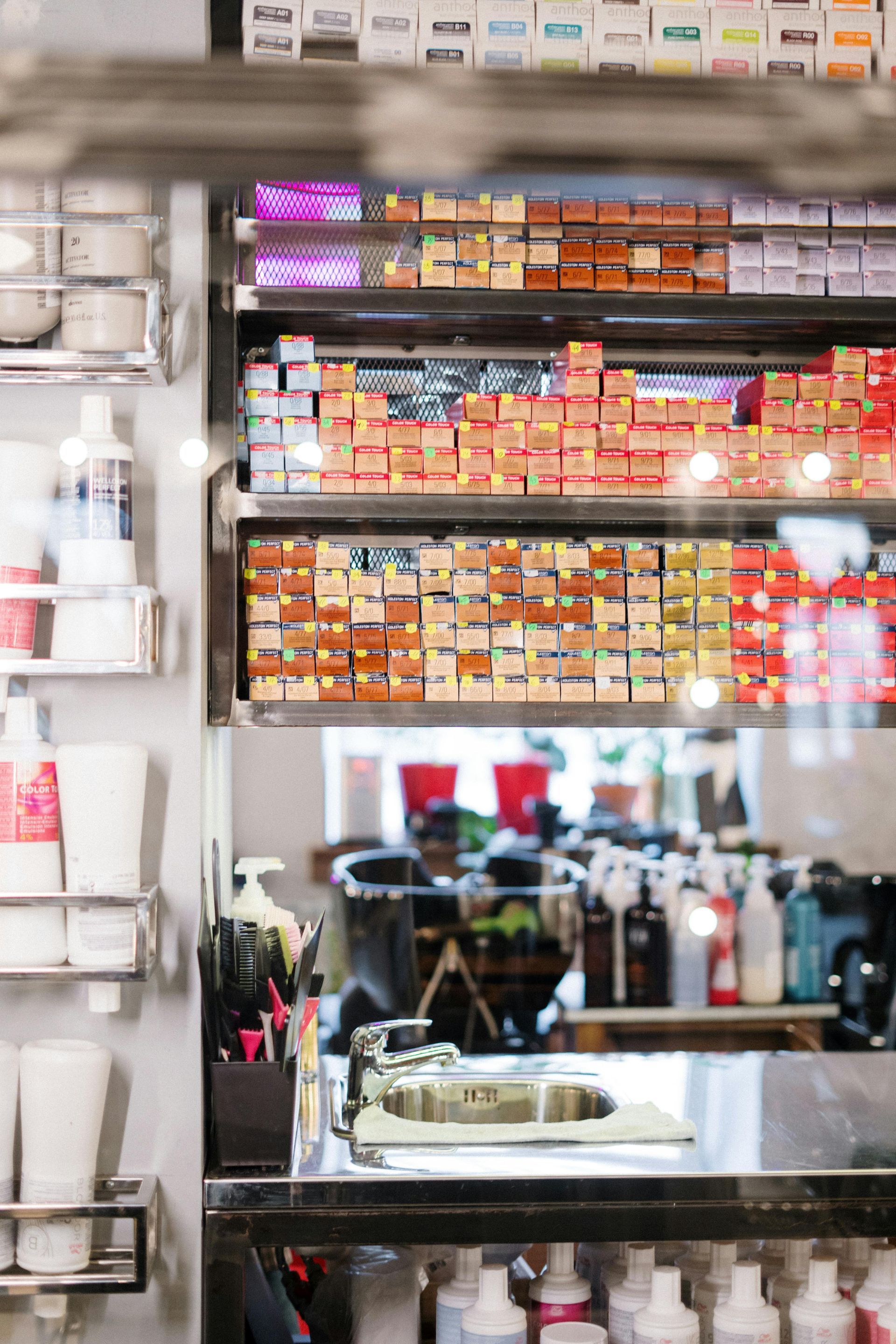 Shelves stocked with hair dye boxes, a salon mirror reflecting a bustling workspace.