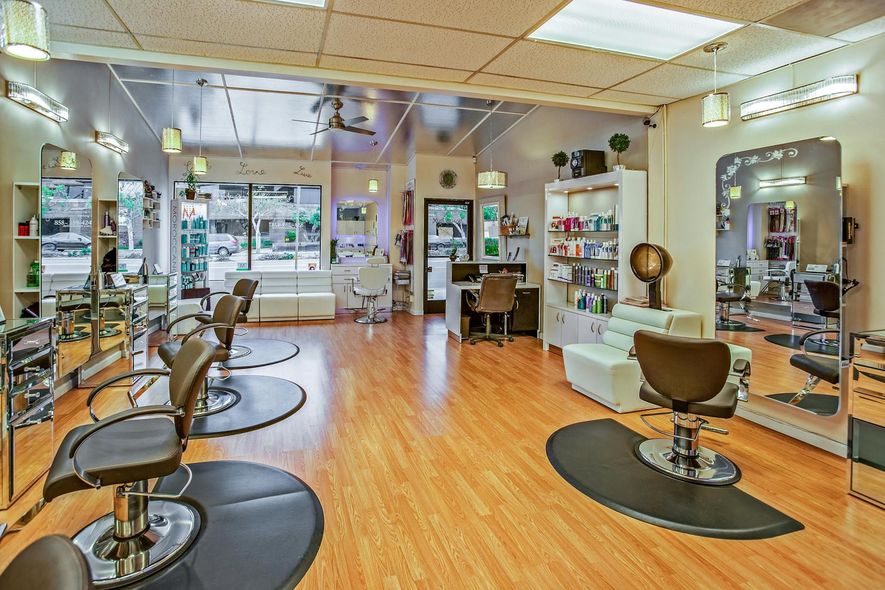 Hair salon interior: chairs, mirrors, products, and a reception desk in a brightly lit space.