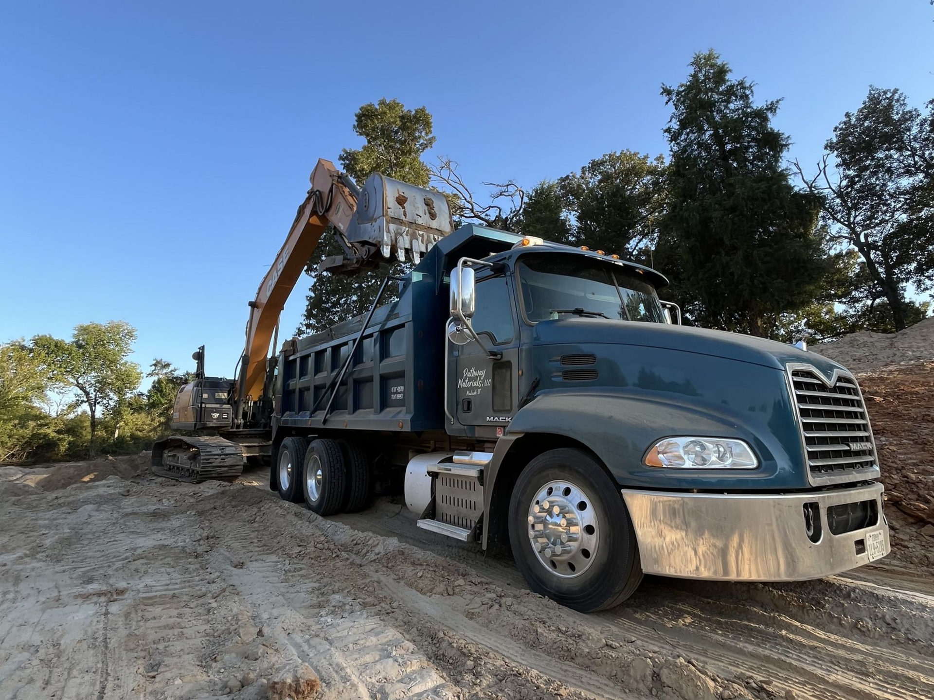 A blue dump truck being loaded with rock by an excavator on a dirt road.