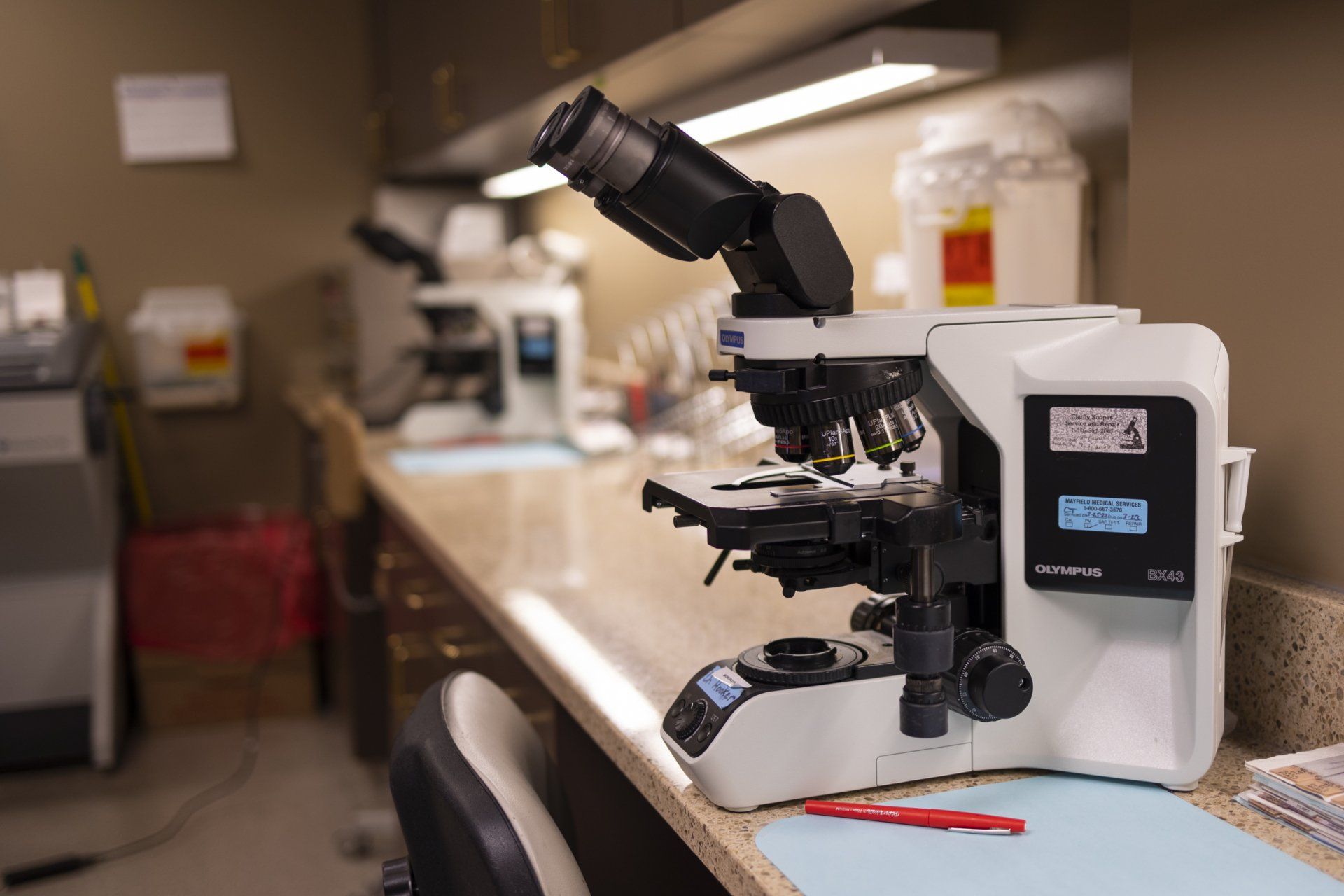 Microscope on a lab countertop, second microscope blurred in background.