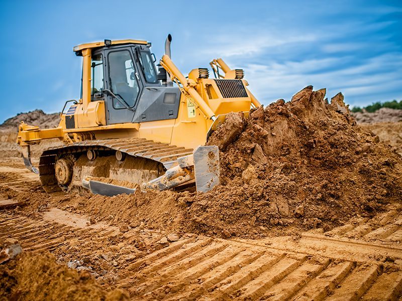 Yellow bulldozer pushing a pile of brown dirt; construction site.