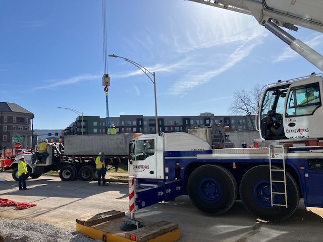 Construction site with a crane lifting a load near a truck and building under a blue sky.
